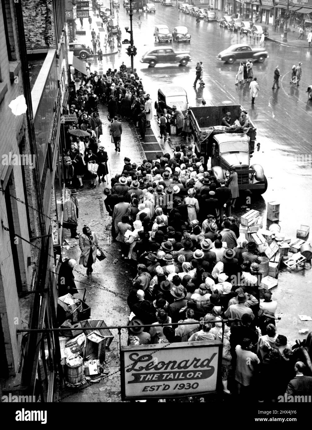 Form in Rain for Chance at Meat - Filling almost the entire width of the sidewalk in front of several stores on Sixth Avenue, between 13th and 14th Streets, these prospective customers wait in the rain for their chance to purchase meat at one of the few New York stores where it is available Oct. 12. Some persons formed the line's beginning at 9 p.m. Oct.11 on the rumor that meat would be places on sale at store opening Oct. 12. October 12, 1946. (Photo by Associated Press Photo). Stock Photo