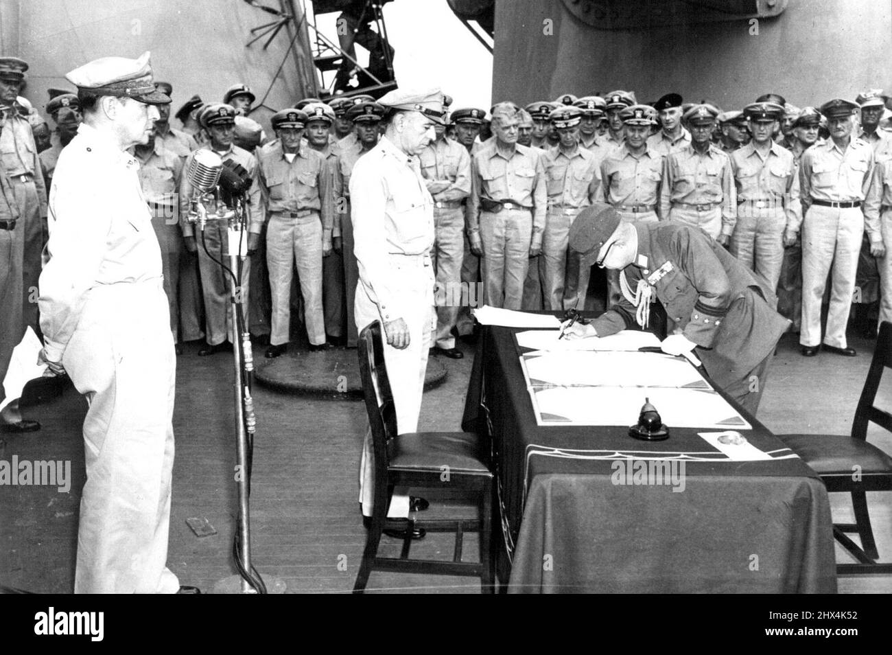 Japanese General Signs Unconditional Surrender Documents -- Japanese General Yoshijiro Umezu, Chief of the Imperial General Staff, signs Japan's surrender documents in the presence of U.S. Lieutenant General Richard K. Sutherland (center), Chief of Staff to U.S. General of the Army Douglas MacArthur (behind microphones), Supreme Allied Commander, and other Allied military officers. The capitulation ceremonies took place aboard the U.S. battleship Missouri in Tokyo Bay, south of the Japanese capital, on Sept. 1, 1945. June 9, 1945. Stock Photo
