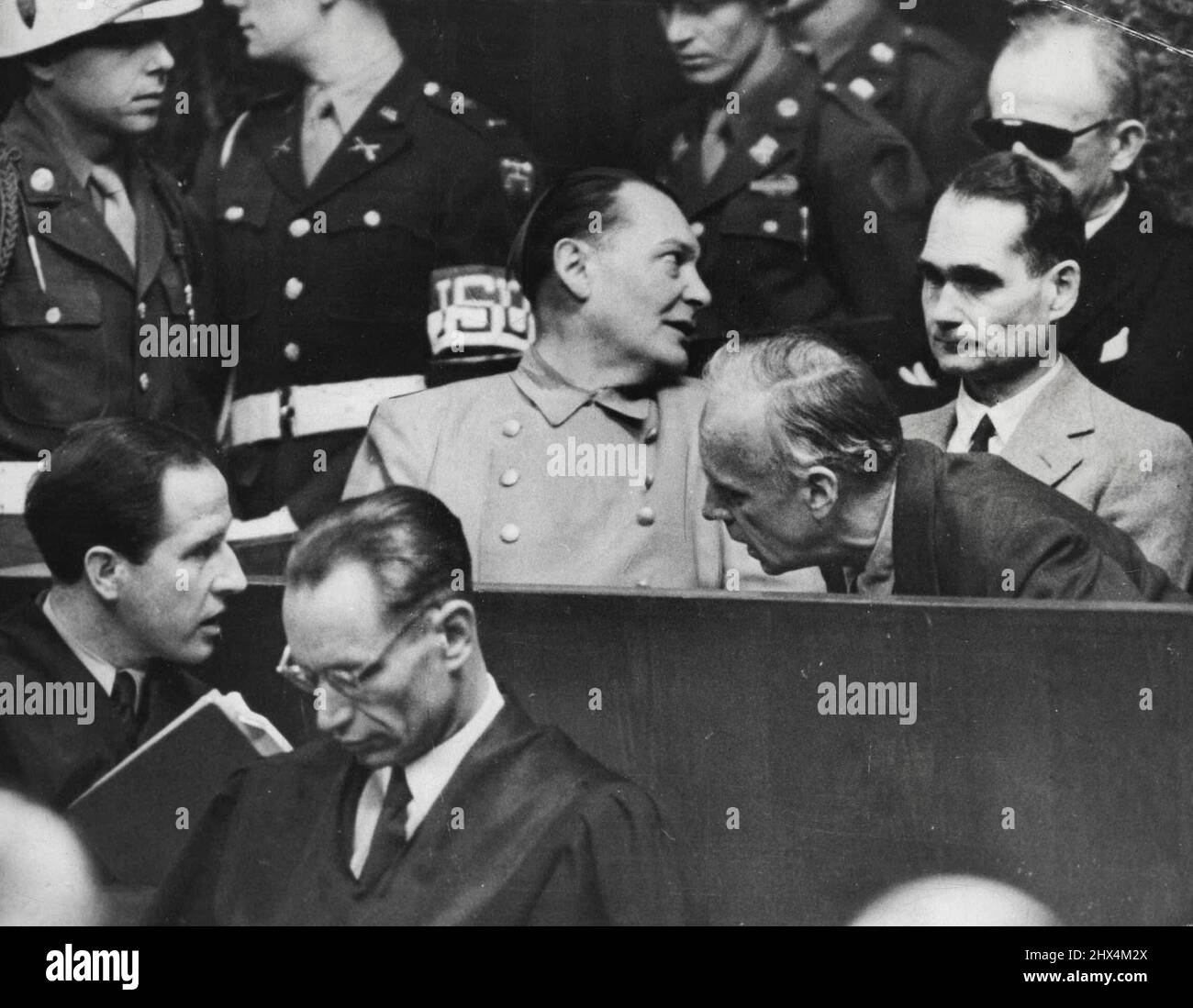 Nazi war criminals whisper in the dock at Nuremberg. Joachim von Ribbentrop leans in front of Rudolf Hess to confer with his lawyer (lower left), whille Hermann Goring (centre), turns to speak to Karl Dontiz (rear right). The trial still drags on. April 18, 1946. (Photo by Associated Press Photo). Stock Photo