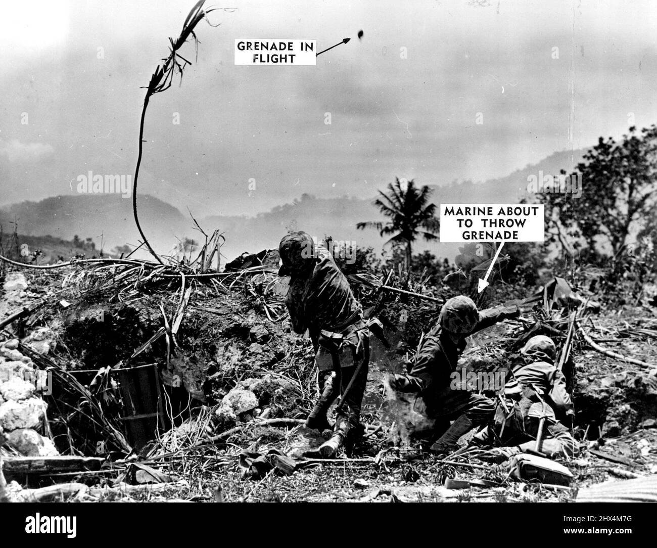 Grenade Hurling Toward Japs A hand grenade, tossed by a Marine (left), sails through the air (top centre), over Saipan; toward a next of Japs. Another Marine (centre), gets set to heave his in the same direction. The second grenade -- the pin pulled -- is giving off smoke, its warning of things to come. July 14, 1944. (Photo by Official U.S. Marine Corps Photograph). Stock Photo