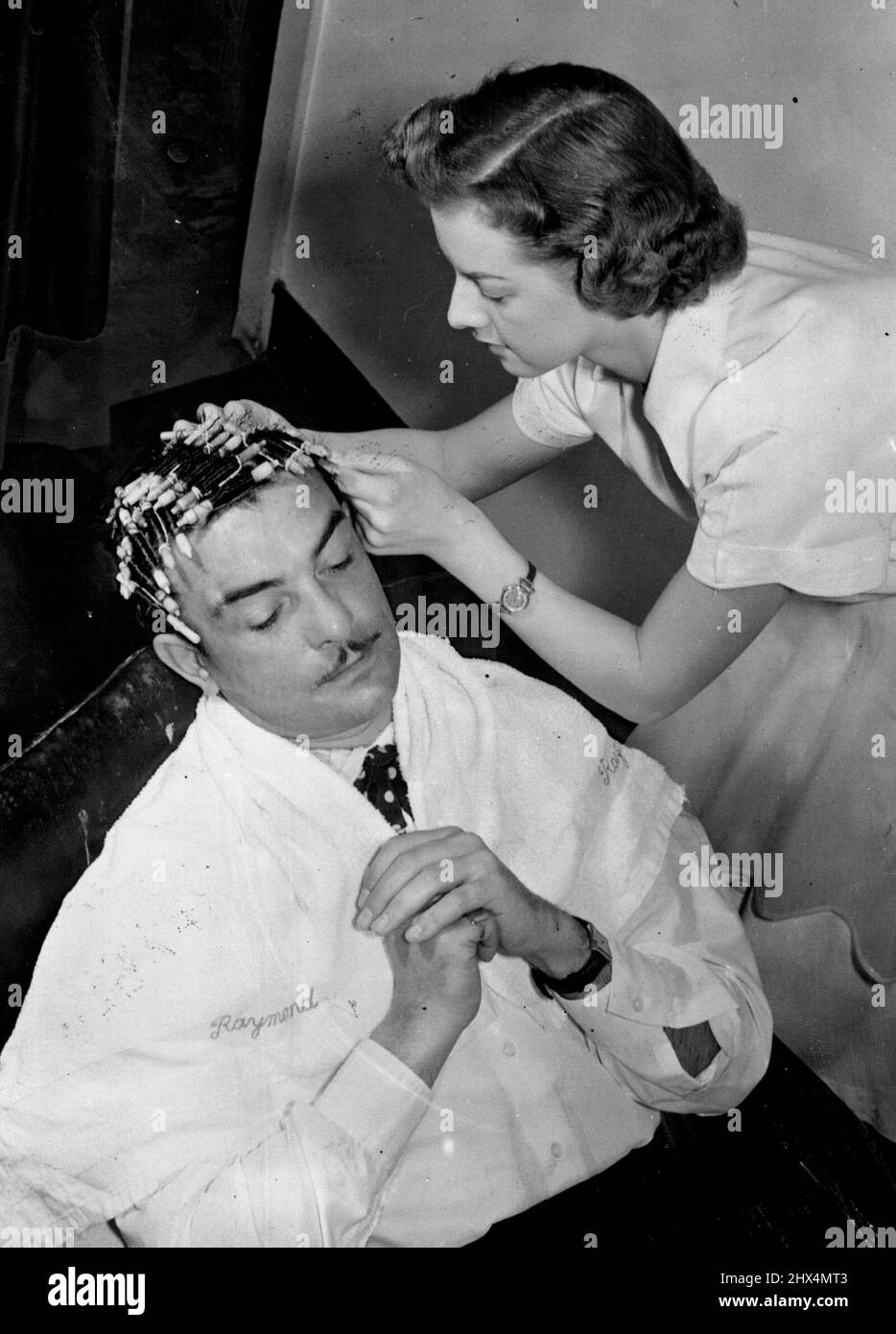 Now, The Poodle Cut - For Men -- M. Raymond looked ever so pretty when his perm was finished and the pins were out. It had taken a long time, and a perm is always wearying, but it was worth it. His head was just a mass of Tony little 'black curls, swept neatly back over the ears. Shaggy - but sweet, M. Raymond, who runs a London women's hairdressing salon, intends to try to persuade others to adopt what he calls the 'Poodle Style. March 09, 1951. (Photo by Daily Mirror). Stock Photo