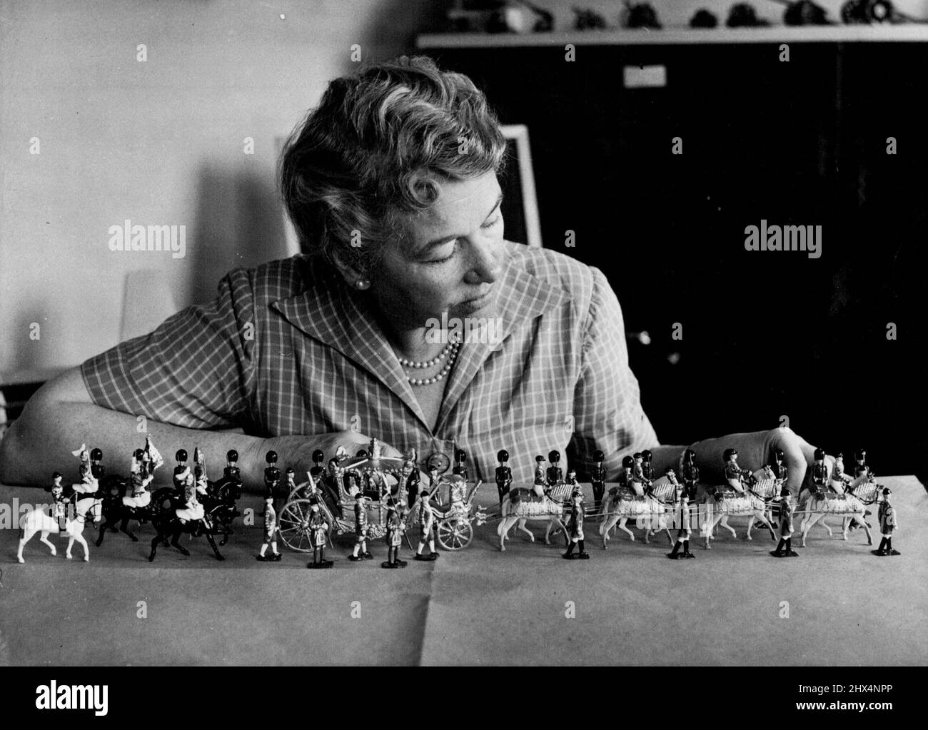 The Coronation Procession in Miniature: Mrs. D.K. Kingswill, of Muswell Hill, photographed arranging the Royal Coach and escort in the miniature Coronation Procession. Makers of toy soldiers and animals, Britains Ltd., have an interesting display which represents the Coronation Procession, complete with Royal Coach and escorting troops. August 27, 1952. (Photo by Fox Photos). Stock Photo