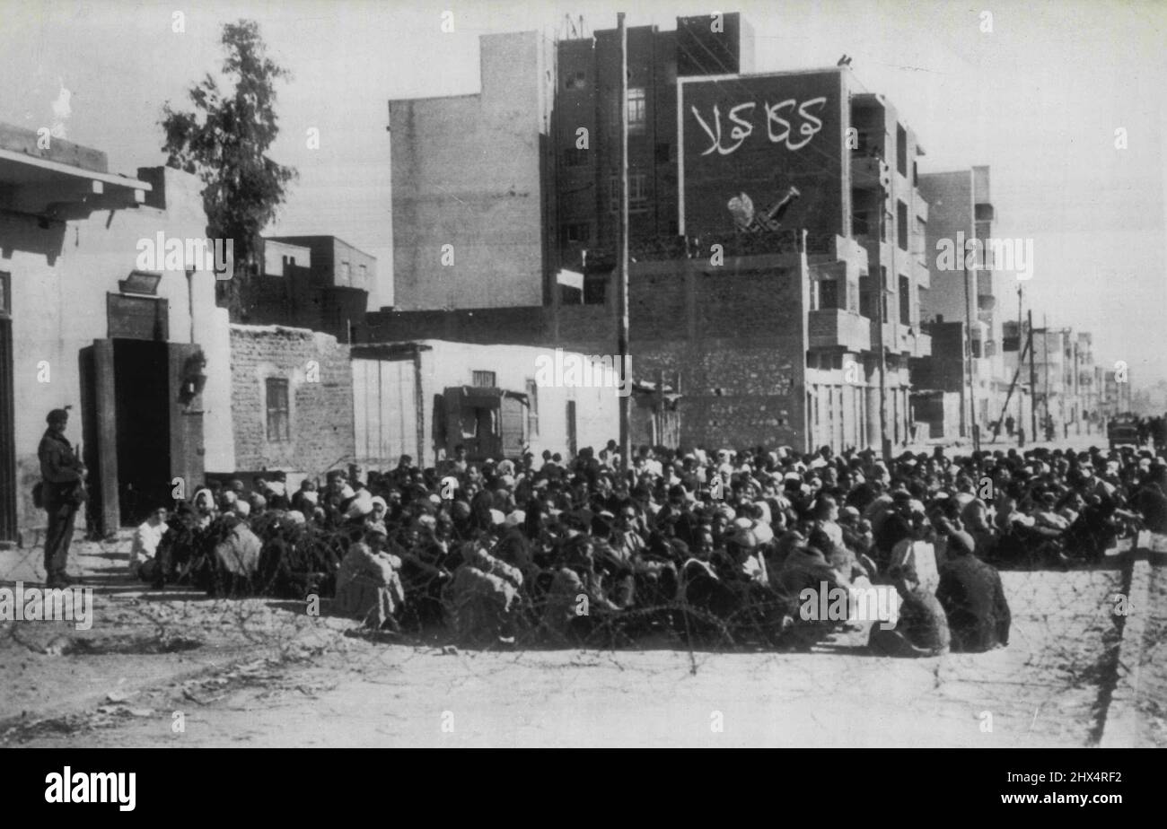 Search For Arms in Egypt - Egyptians sit in a barbed wire enclosure in a street in Ismailia, Egypt, January 22, during a screening and search of homes for arms and ammunition by British 16th Parachute Brigade troops. The British took over in Ismailia after an American nun was killed In a skirmish with Egyptian guerrillas. New fighting broke out yesterday and continued for six hours. January 26, 1952. (Photo by AP Wirephoto). Stock Photo