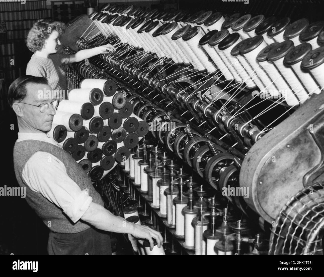 Sheep Supp. -- At John Vicars Pty Ltd Marrickville. In the drawing department, this is the roving operation. The operator at rear is watching the combed wool being drawn into fine slivers ready for spinning, while the man collects the full spools from the machine. May 28, 1952. (Photo by Frank Albert Charles Burke/Fairfax Media). Stock Photo