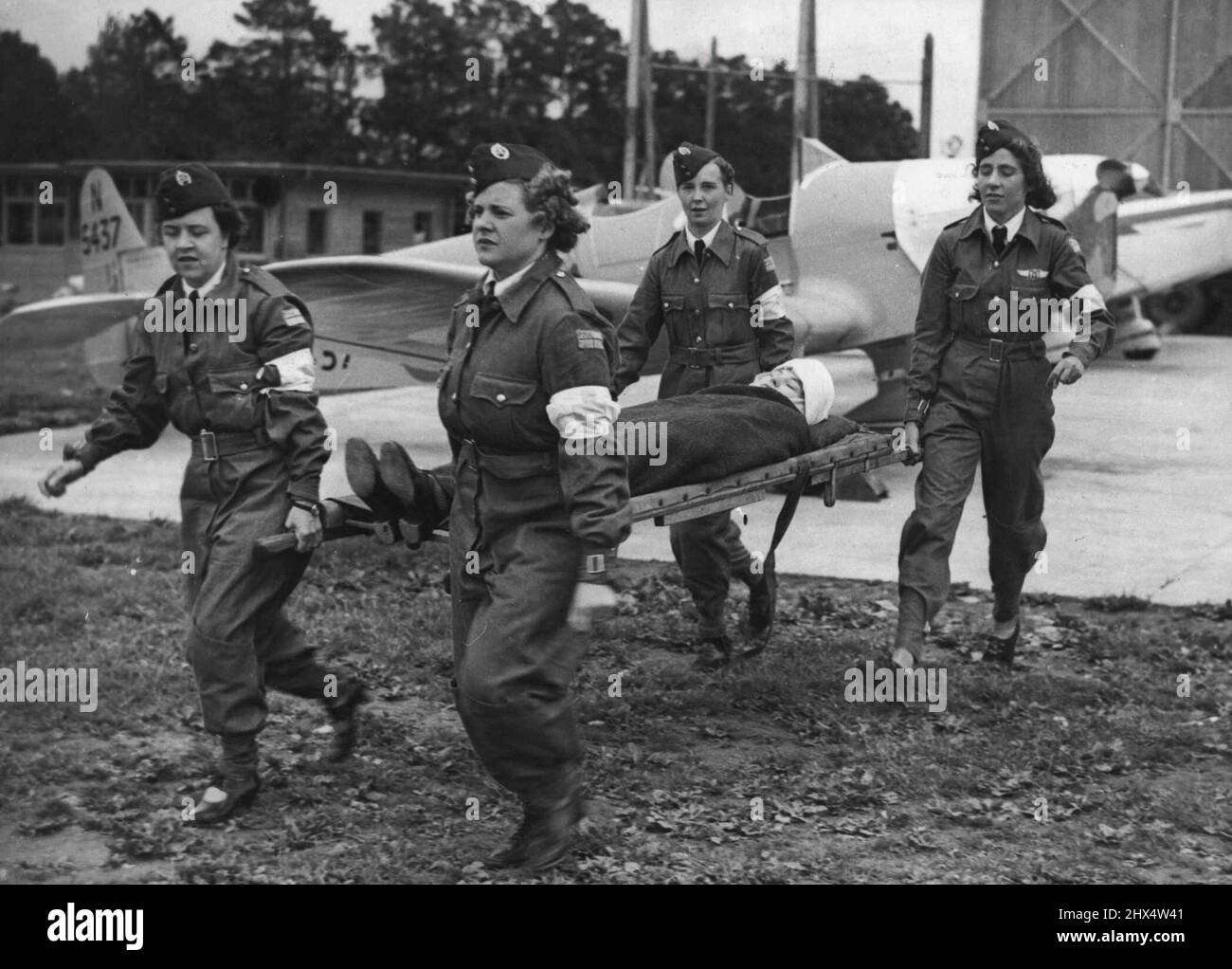 Civil Air Guard Girls Demonstrate - First Aid Members of the Civil Air Guard carrying the 'Victim' of a flying accident, off the Aerodrome at Plymouth, on a stretcher. The section of 'The Civil Air Guard which is stationed at Plymouth Aerodrome, has a woman's ambulance section. These girls have been learning first aid from a qualified nurse and are specially learning how to deal with those injured in flying accidents. July 26, 1939. (Photo by Keystone). Stock Photo
