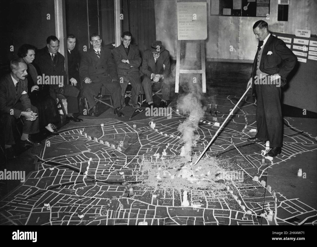 Floodlit Model Aids Civil Defense Training -- Members of The Camberwell Civil Defense receiving training with the aid of the at their floodlit floor model, at their Depot in Vale End, East Dulwich. In the center is Mr. F.W. Dyson, the instructor, who has made the wooden models for this scheme in is spare time, pointing out a realistic incident in the center of the Borough, the effect of which is aided by smoke. A new Civil Defense training method has been introduced in the Borough of Camberwell and other Boroughs throughout London are expected to follow it's lead. February 2, 1954. (Photo by F Stock Photo