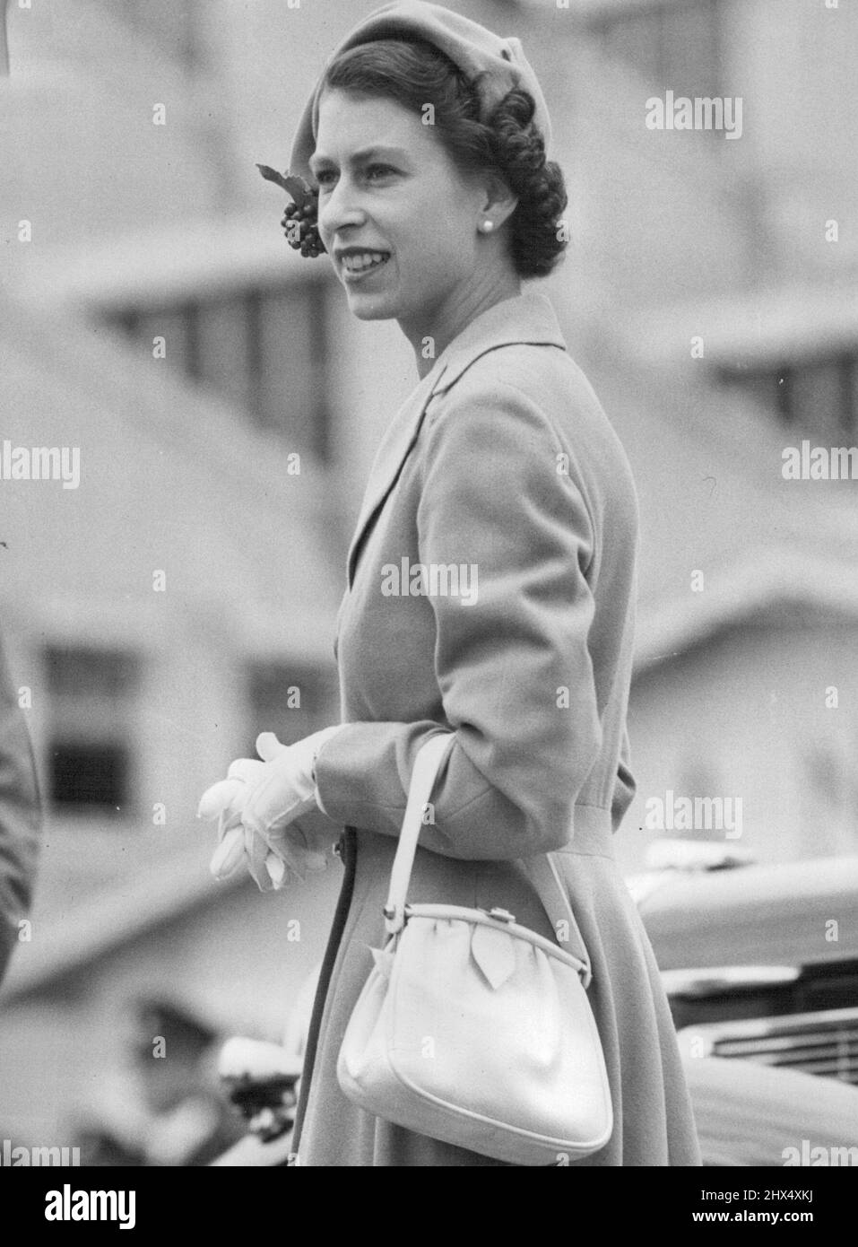 Royal Tour Pictures - 1954. Perfectly groomed as usual, the Queen in this picture stepped from the Royal car at Perth airport today for the formalities preceding her take-off for Busseltone She wears a soft green fitted coat of. fine wool with slightly flared skirt, over a printed summer dress. There is a small matching cloche hat trimmed with a bunch of cherries. Accessories are white. April 2, 1954. Stock Photo