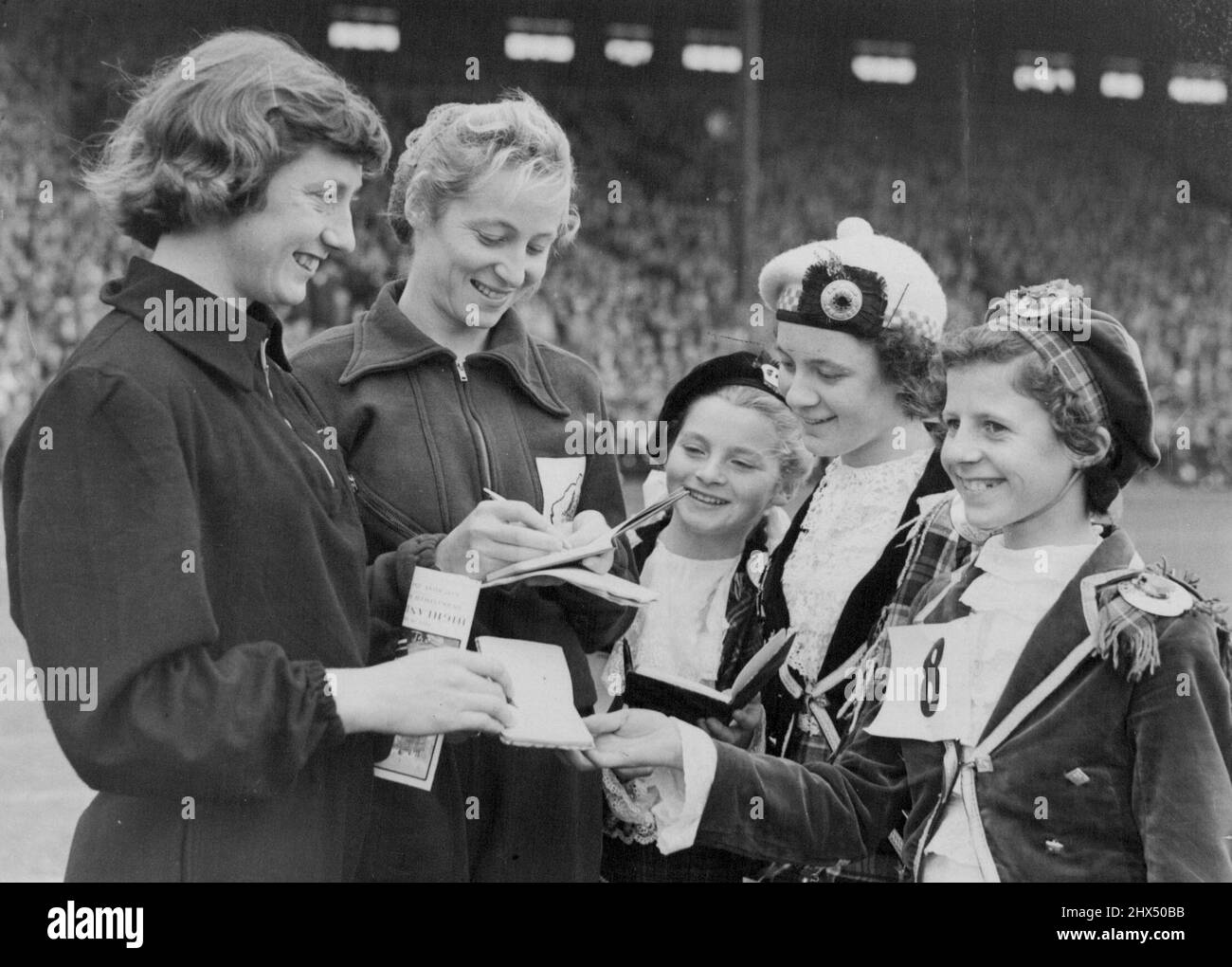 Olympic Stars Sign Up -- These little Highland dancers claimed autographs from Olympic Gold Medalists Yvette Williams of New Zealand (long jump), at left, and Australian Shirley Strickland (80 metres hurdles), during the annual City of Edinburgh Highland Games, staged at Murrayfield Rugby Ground. August 25, 1952. Stock Photo