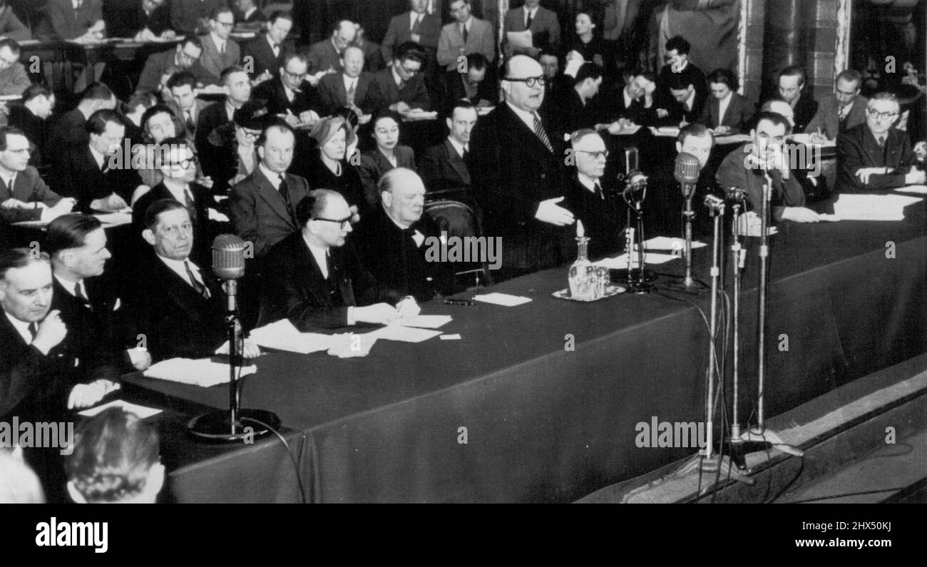 Spaak Opens European Movement Conference -- Belgium's Premier Paul-Henri Spaak (standing) opens the first session of the Council of the European Movement at the Palais des Academies in Brussels, Feb. 25. Listening at his right is Winston Churchill who yesterday made a fiery plea for European unity in a Communist-heckled speech before the Council, an unofficial organization aiming towards a United States of Europe . At the table (ltor): Robert Bichet of France; Hendrik Brugmans of Holland; J.H. Retinger of Poland; Guy Mollet of France; Churchill; Spaak; Meuccio Ruini of Italy; Duncan Sandys, pr Stock Photo