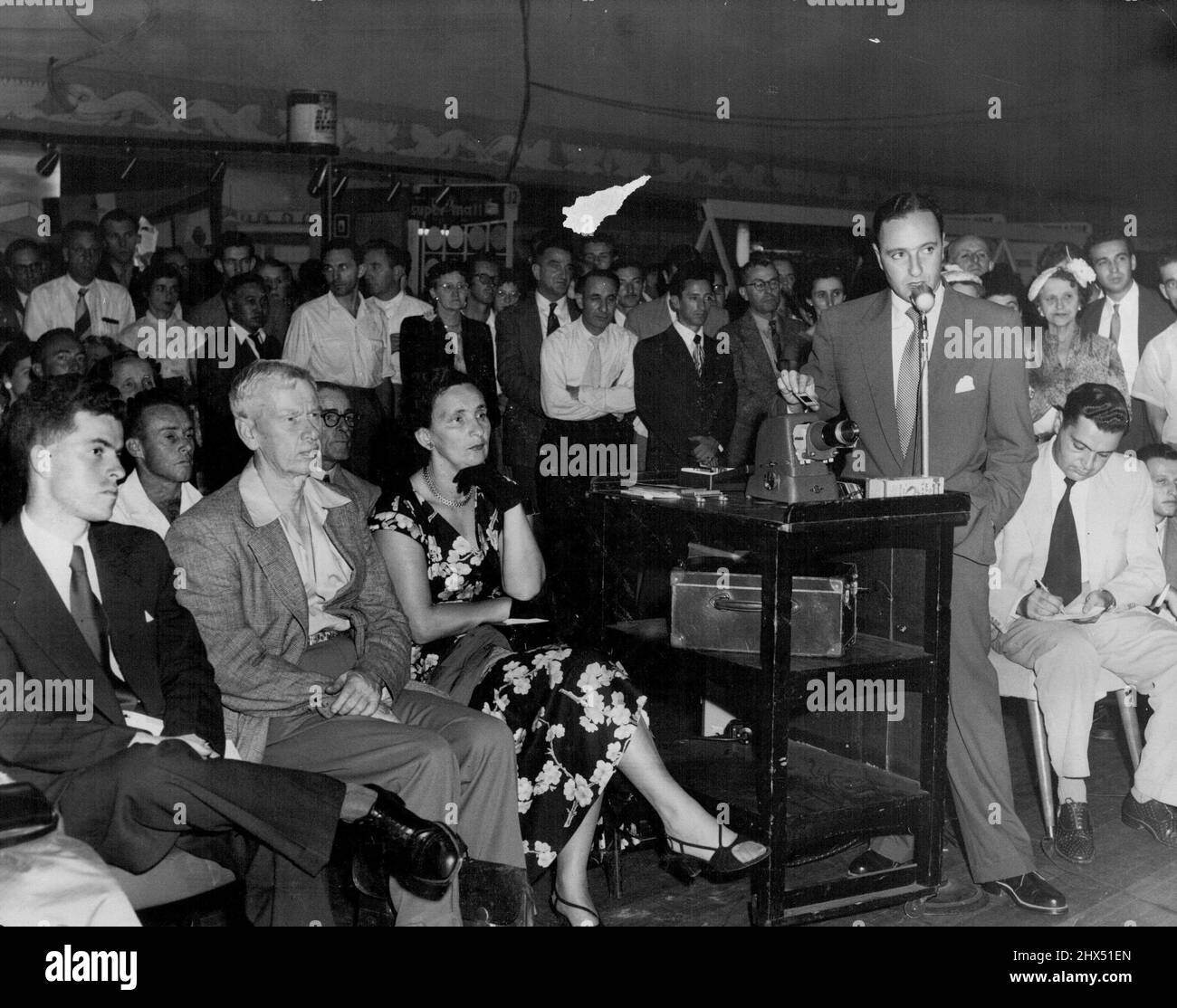 Harry Seidler, well known architect (speaking into microphone),lecturing to large crowd on modern architecture at the Building and Housing Exhibition at the Trocadero to-night. Seidler is using a strip film projector to illustrate his lecture. February 09, 1955. (Photo by Leyden). Stock Photo