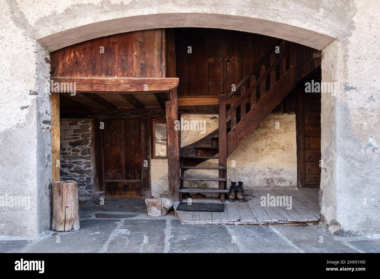 Close-up of portal in white rendered stone wall with wooden panel entrance and staircase and leather boots and clogs placed outside in Chamonix France Stock Photo