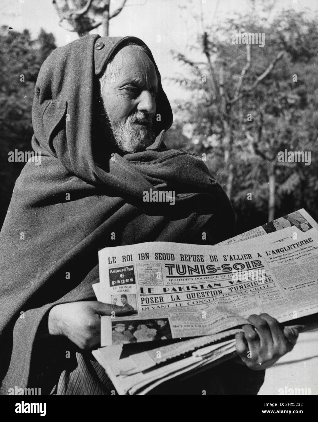 A Hooded Arab 'Newsboy' hawks one of the French Language newspapers in a screeching voice in downtown Tunis. Note that the headline plays up king lbn Saud's Rejection of alliance with England. February 29, 1952. (Photo by United Press). Stock Photo