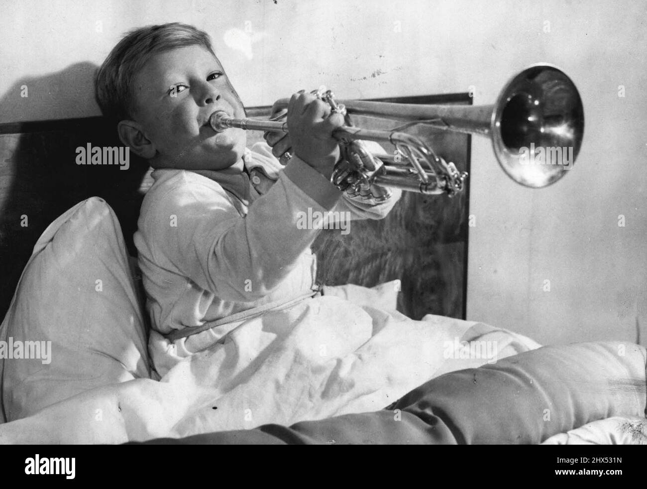 Young Man With A Horn -- A puffy-cheeked young man with a £22 silver trumpet may some day be the successor of Louis Armstrong and Harry James. He is 4-year-old Roger, son of Mr. and Mrs. Thomas Sawell of West Wickham, Kent -- pictured here in his bed, blowing high hard 'early morning' notes on his shiny instrument, as he does every morning at six o'clock. Mr. and Mrs. Sawell don't find it necessary to set their alarm clock. Roger has been blowing the trumpet since he was two years old, and his music teacher, Mr. E.G. Moss, ***** he can already play nearly as ***** as most youths of twenty. Nov Stock Photo