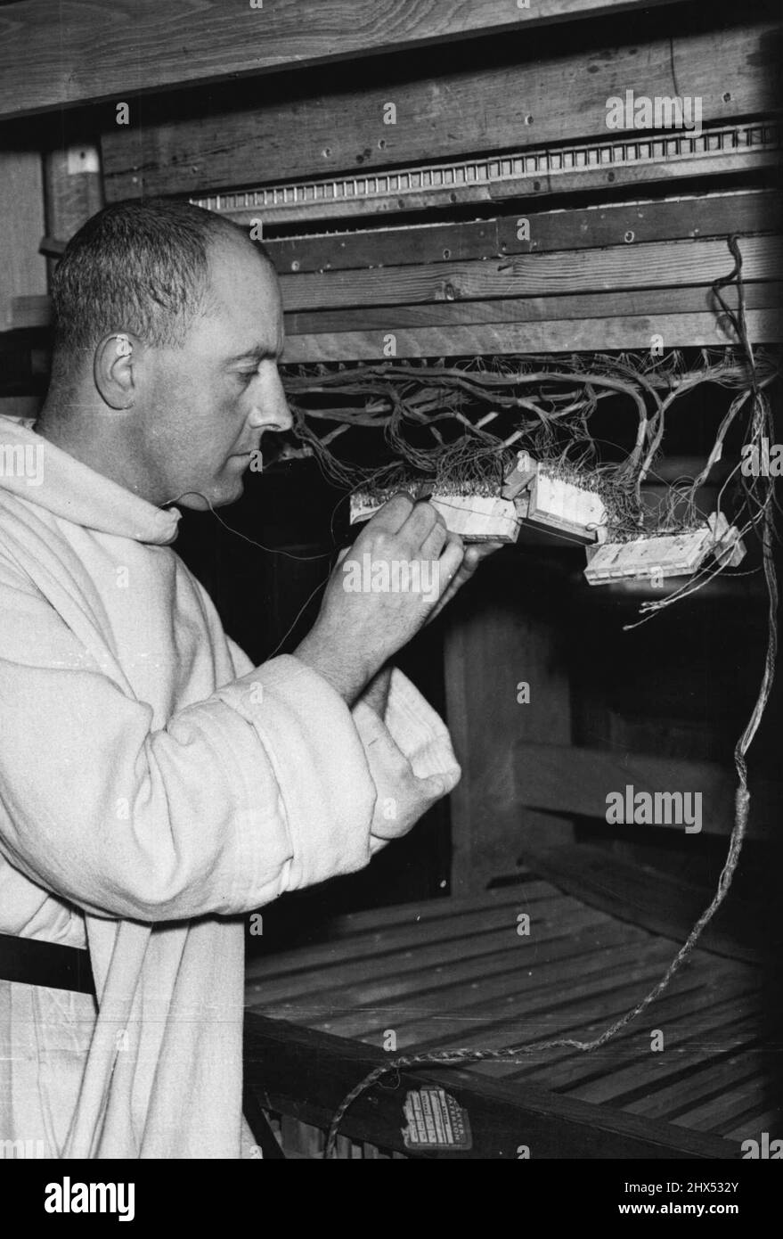 Monk Builds Organ: A close-up of Dom Ethelbert Watson, O.S.B. seen at work on the wiring of the electrical relay system of the nearly completed organ he is building for Prinknash Abbey. When completed, about 19 miles of wire will have been used on the organ.After 4 years work, Dom Ethelbert Watson O.S.B., of Prinknash Abbey, near Gloucester, is nearing completion of a 400 pipe all-electric extension organ, of his own design, for the Abbey Chapel. The electric mechanism is a modern development, but the organ has the tone of the 17th. Century Baroque period. October 15, 1955. (Photo by Fox Photo Stock Photo