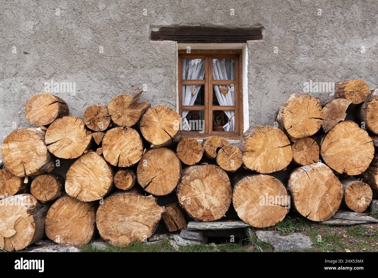 Large cut timber firewood logs stacked against the grey rendered wall of a rustic farmhouse in Chamonix France Stock Photo