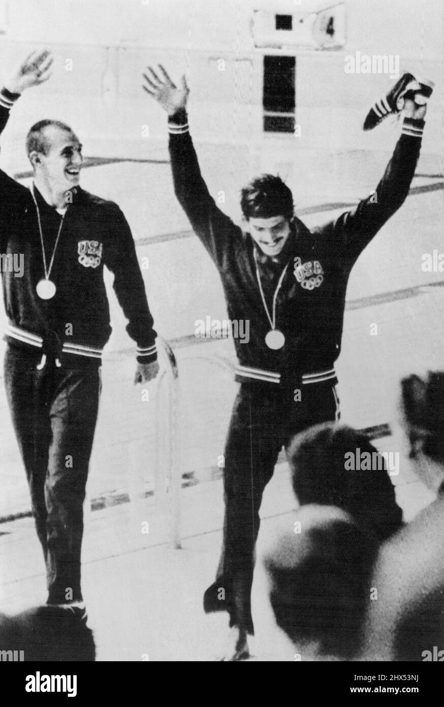 Carrying his shoes, record breaking gold medal swimmer Mark Spitz joins U.S.A. teammate Steven Genter(L) in waving to crowd after accepting medals that hang around their necks. presentation followed 200 meters freestyle in which Spitz set new world record of 1:57.78 Genter took second; W. German Werner Lampe was third, beating Australia's Wenden, who was fourth. April 8, 1929. (Photo by UPI) Stock Photo