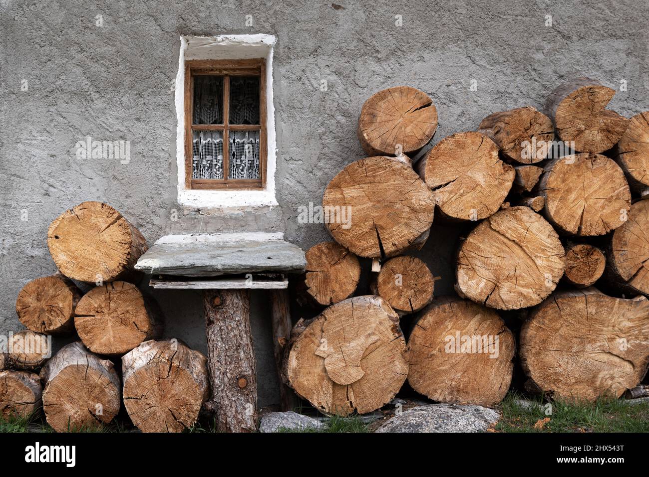 Large cut timber firewood logs stacked against the grey rendered wall of a rustic farmhouse in Chamonix France Stock Photo
