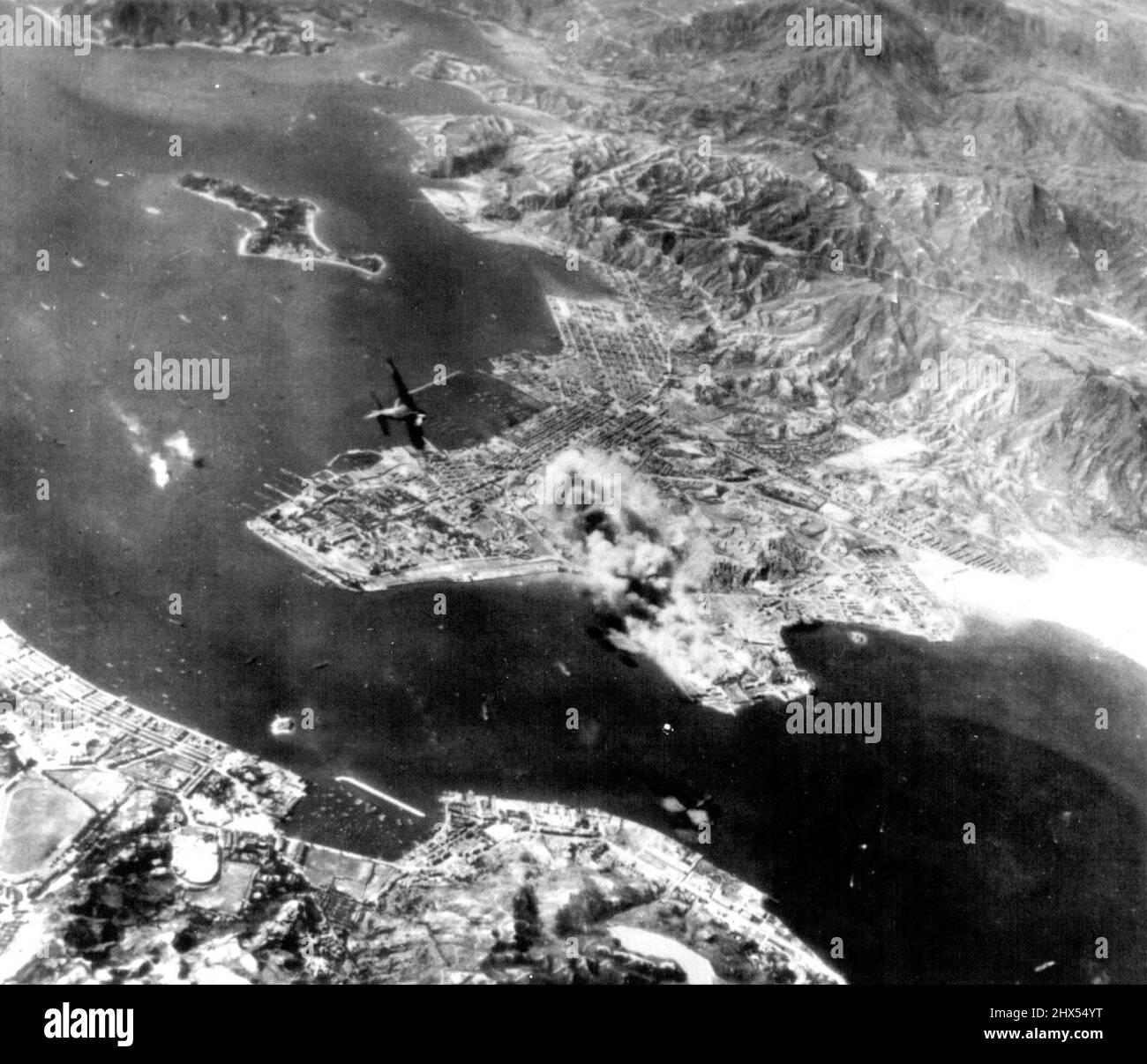 Yanks Hit Hong Kong Harbor In Surprise Attack -- Smoke ***** up from Kowloon docks and Railroad yards under the surprise ***** attack on Hong Kong Harbor October 16 by the U.S. army 14th ***** A Japanese fighter plane (left center) turns in to ***** Between the Royal Navy Yard (left) and Stonecutter's ***** Enemy vessels spout flames, and just outside ***** another ship has been hit. This attack sank ***** October 26, 1944. (Photo by AP Wirephoto). Stock Photo