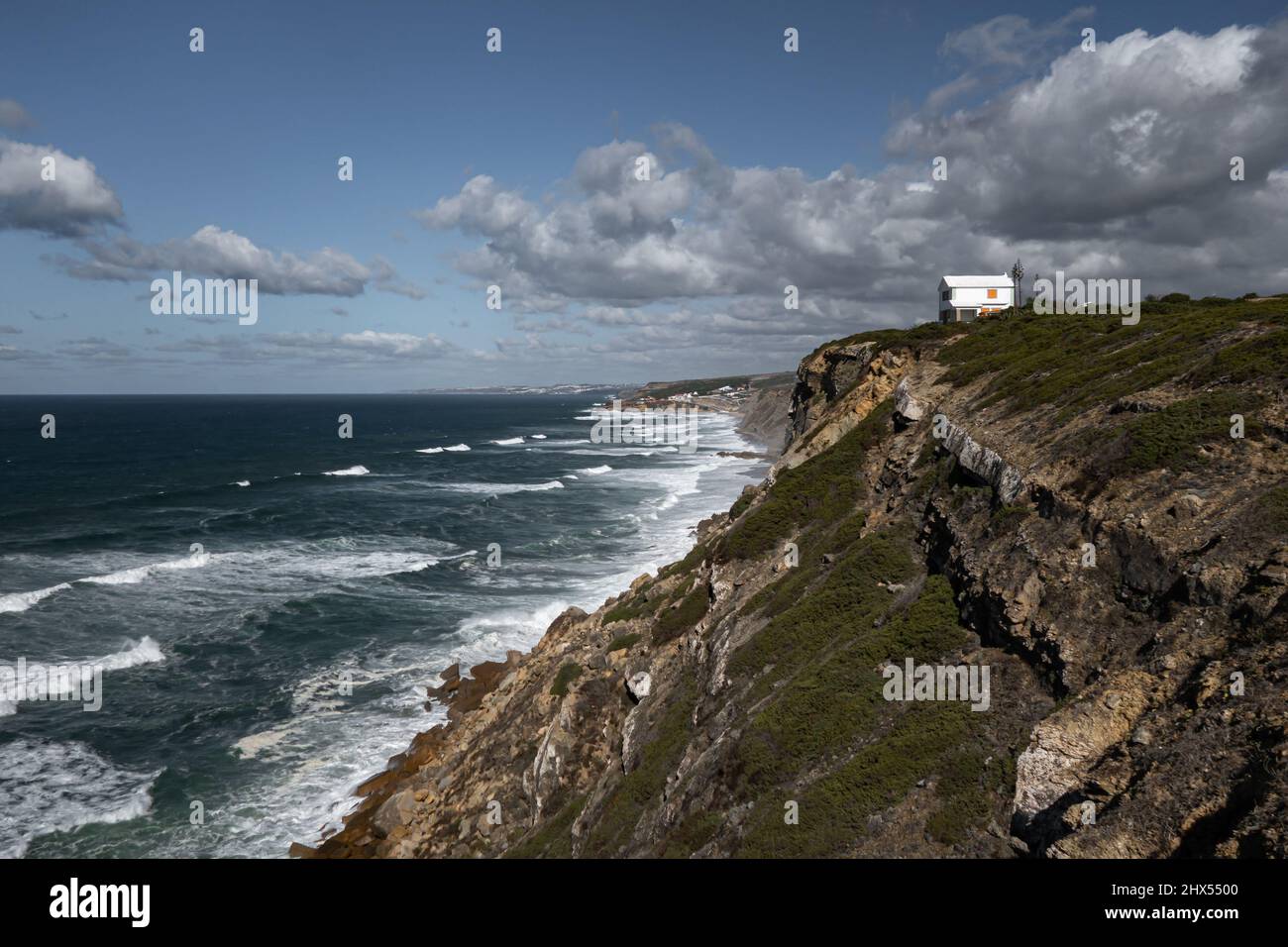 Panorama of white rendered wall summer house situated on cliff edge overlooking the Atlantic Ocean with rolling waves on Sintra coastline in Portugal Stock Photo