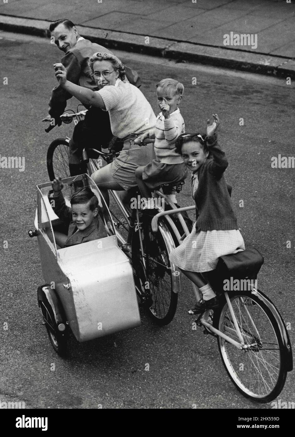 A 'Carriage' For Five Mr. Eric Jewell of Finchley, London, was fed up with queueing for buses with tired children, so with his wife, he went back to his hobby of cycling. He built a sidecar and added to his tandem - bicycle. But this was not enough to hold all the family so half a bicycle was tacked on behind and an extra saddle and a pair of hadlebars placed behind mother - now he has a quinticycle made for five and the family are all happy as they travel around together. August 08, 1950. (Photo by Paul Popper Ltd.). Stock Photo