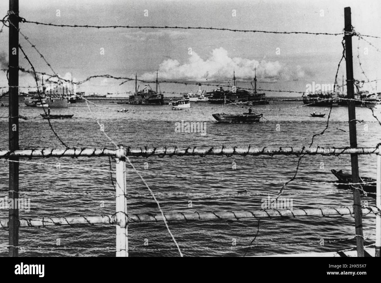 Barbed wire entanglements along Singapore's Waterfront frames this view of the Harbor. Cross roads of the far East, The port is always crowded with shipping. most of the tin and much of the rubber imported from the East Indies by the United States, is shipped via Singapore. November 14, 1941. (Photo by ACME). Stock Photo