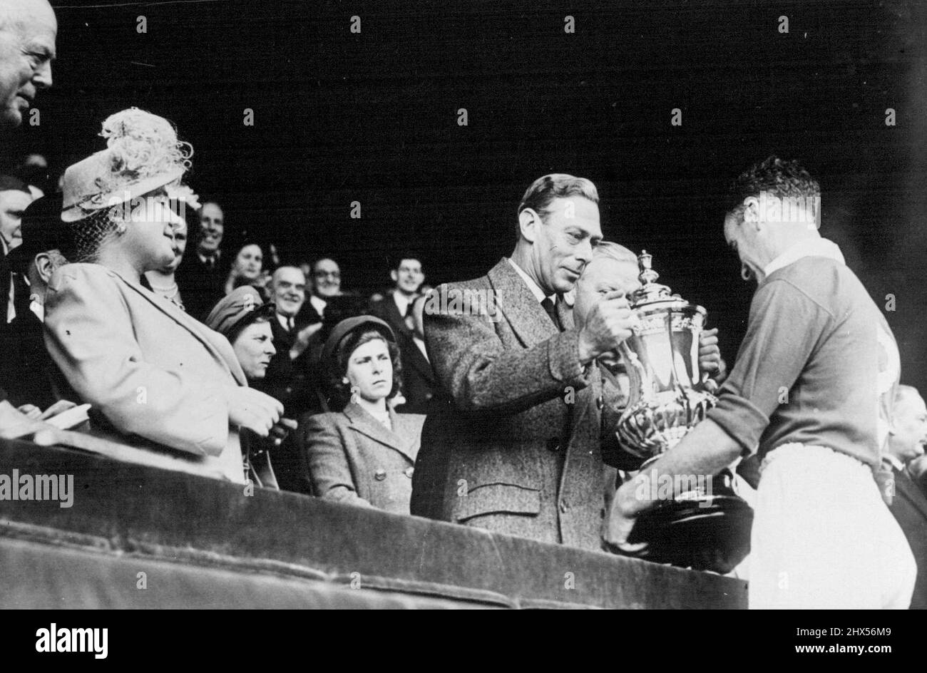 Manchester United Win The Cup -- The Queen smilingly looks on as H.M. The King presents the Cup to Carey, the Manchester United captain. Before a record crowd at the great Wembley Stadium, London, Manchester United defeated Blackpool by 4 goals to 2 and thus won the F.A. Football cup. April 24, 1948. (Photo by Sport & General Press Agency Limited) Stock Photo