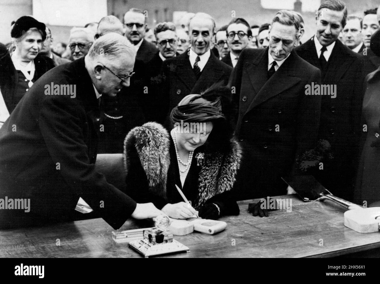 The King and Queen Visit The East End of London. H.M.The Queen, watched by the King, autographs the spade with which she had planted a Maple tree in the grounds of a new School on the site.Their Majesties the King and Queen were given a great welcome when they visited the London County Council reconstruction scheme at Lansbury, Poplar, east London. The scheme covers about 124 acres most of which were destroyed by enemy bombing during the war. Model flats, houses and shops will occupy the site while part has been reserved for Exhibitions of Architecture for the 1951 Festival of Britain. Novembe Stock Photo