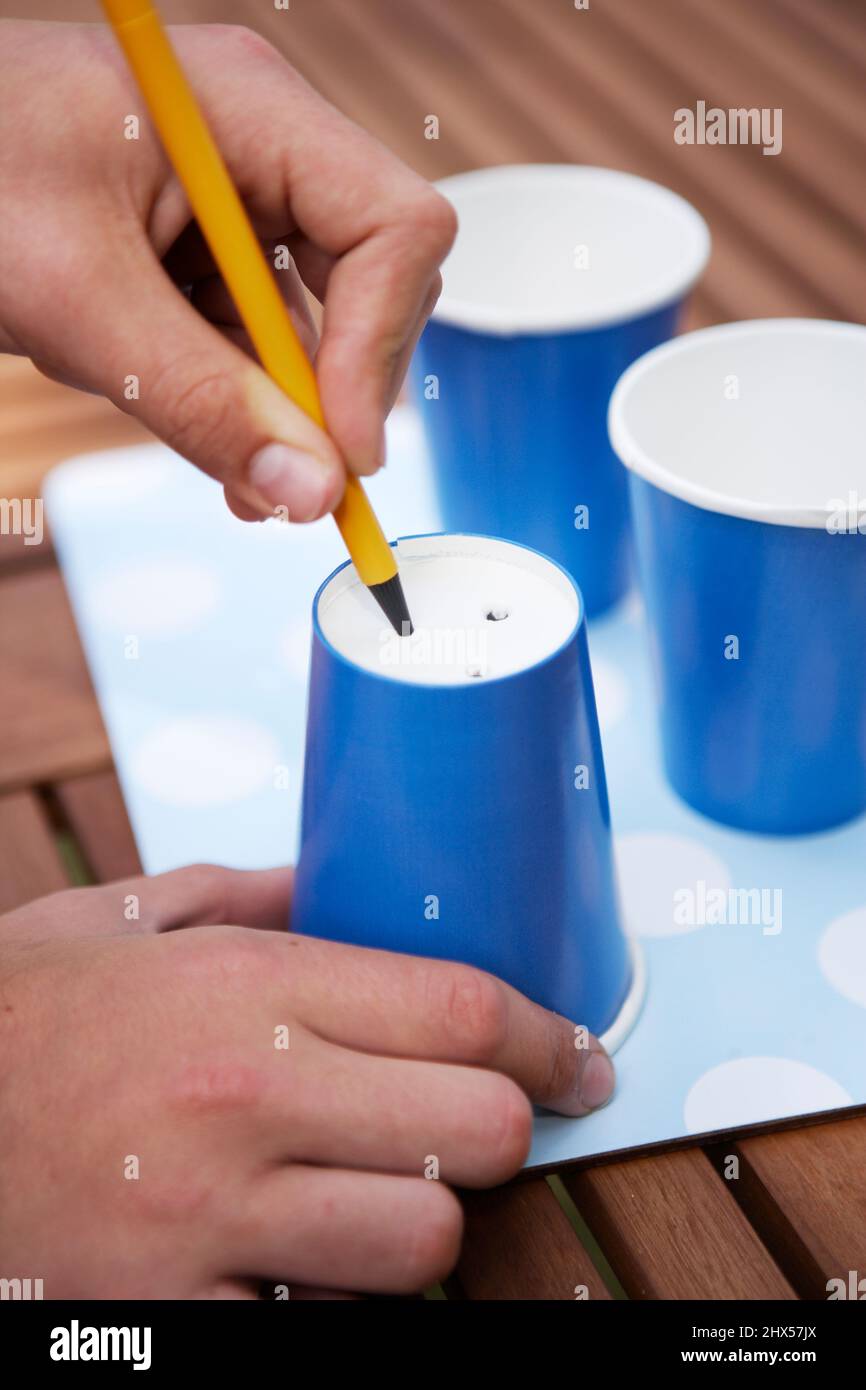 Person making holes in the base of a paper cup using a pencil Stock ...