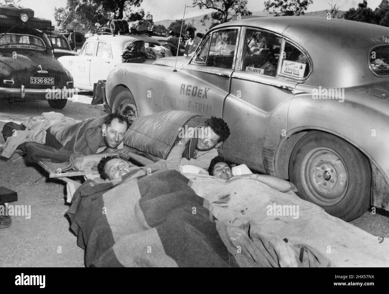 Tired, but still smiling -- Jaguar crews settle down to sleep beside their cars in the Alice Springs control area. The men are Noel Sweeney, Bob Hutchison, Eric Staples and Dan Mott. September 11, 1953. Stock Photo