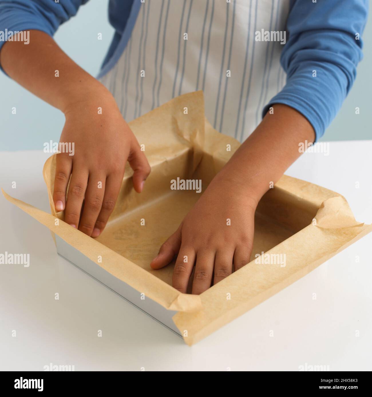 Boy lining square cake tin with greaseproof paper, closeup Stock Photo