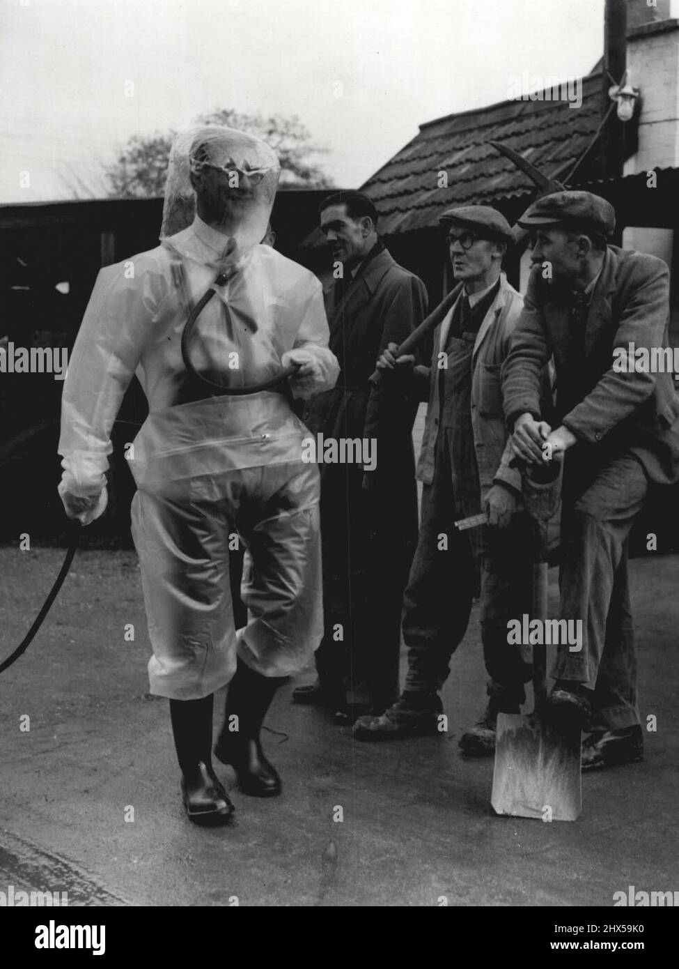 Britain's Anti-Atom Suits -- Workmen gape as what is undoubtedly a visitor form outer space strolls through the quiet of Woburn Sands. Buckinghamshire, today November 19. The "Spaceman" was giving a demonstration of the New Plastic Suits which are being produced by a plastics factory at Woburn Sands to give protection from atomic dust to workers at Britain's Atomic Factories. Inside the Bubble Hood of the welded-seams suit the wearer breathes pure air pumped in by a compressor. The Suit, silver-grey in colour and weighing only 3½ pounds, costs less than £10. American atom officials are Stock Photo