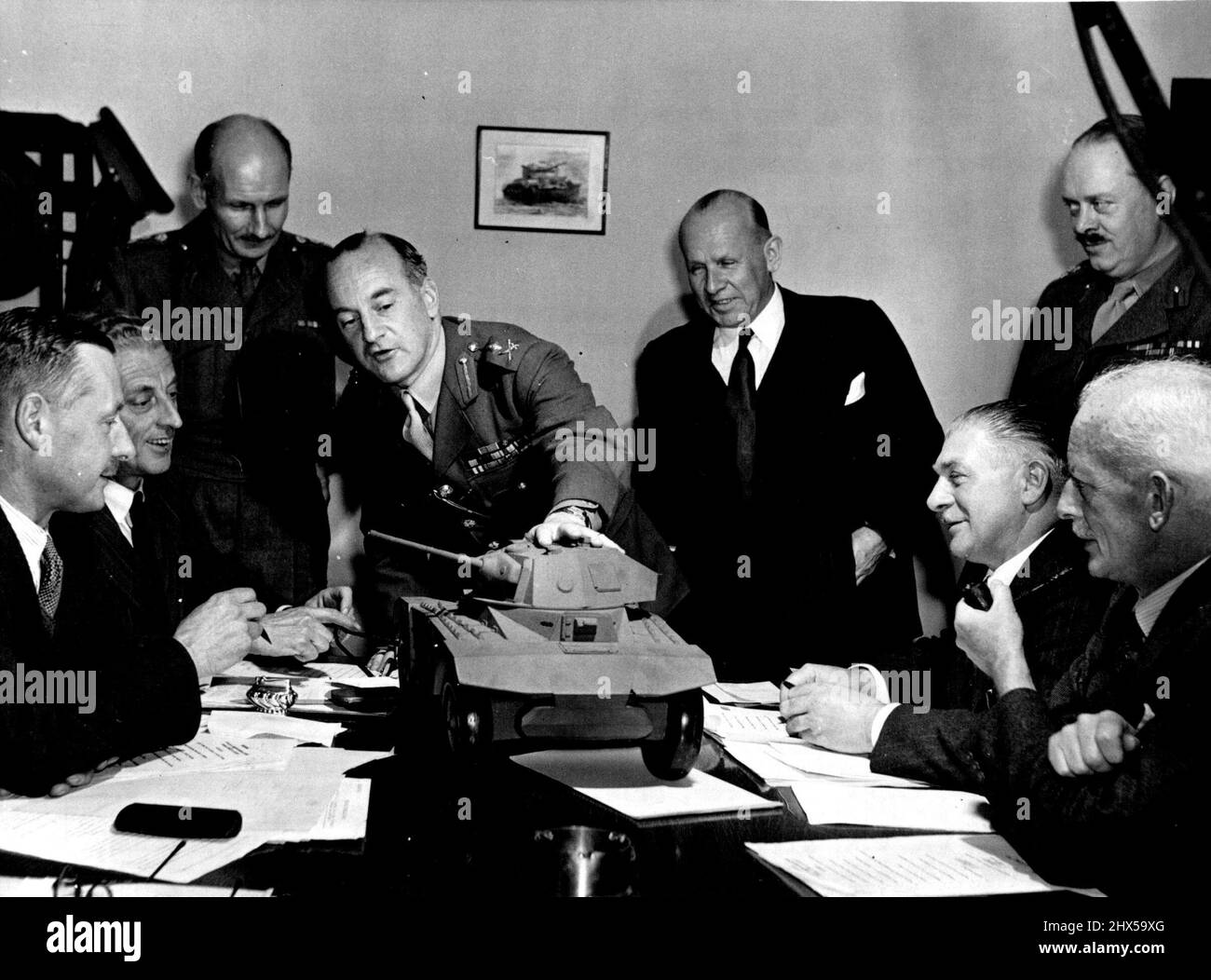 Take Expert Heads Production Team -- Major. General H.E. Pyman is Director-General of Fighting Vehicles.Here Major General Pyman President at his monthly conference at the Ministry's Tank proving and Experimental establishment. Technical experts listening to him enumerating points about an armoured car model are: (left to right) Brig. O.E. Chapman, Chief Inspector of Fighting Vehicles, Mr. A.E. Masters, Chief Engineer, Brig. S.R.W. Clarke, Chief of the Fighting Vehicle Proving Establishment, Major General H.E. Pyman, Mr. W.E. Millar. Director of wheeled vehicle Production, Brig. W.S. King, Dir Stock Photo