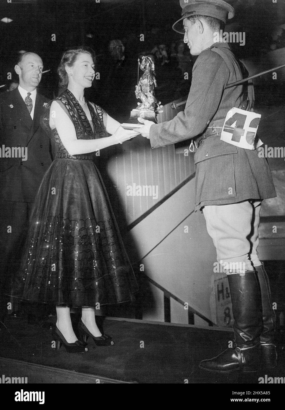 So The Cup Changes Hands - Princess Elizabeth, in a dark spiral-embroided evening dress presents the George V Gold Challenge Cup to Capt. K. Barry of the Eire Army, at the International Horse Show, at the White city, London last night. Captain Barry on his chestnut mare Ballyneety, had the only clear round in the finals. Lt. Col. Harry Llewellyn, Winner in 1948 and last year, came to grief on a white wicket gate which proved the 'graveyard' of many hopes during the evening. Lt. Col. Harry Llewellyn was riding Foxhunter. July 26, 1951. (Photo by Paul Popper). Stock Photo