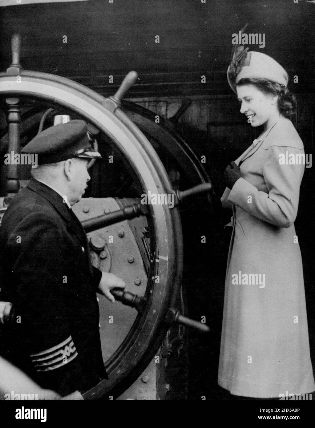 Princess Takes The Wheel - H.R.H. Princess Elizabeth takes a close look at the great steering wheel of the New Zealand four masted barque Pamir, during her visit with the Duke of Edinburgh to the ship in Shadwell Basin. The ship's master Capt. H. Collier is explaining the mechanism,- to-day (Wednesday). March 3, 1948. (Photo by Reuterphoto). Stock Photo