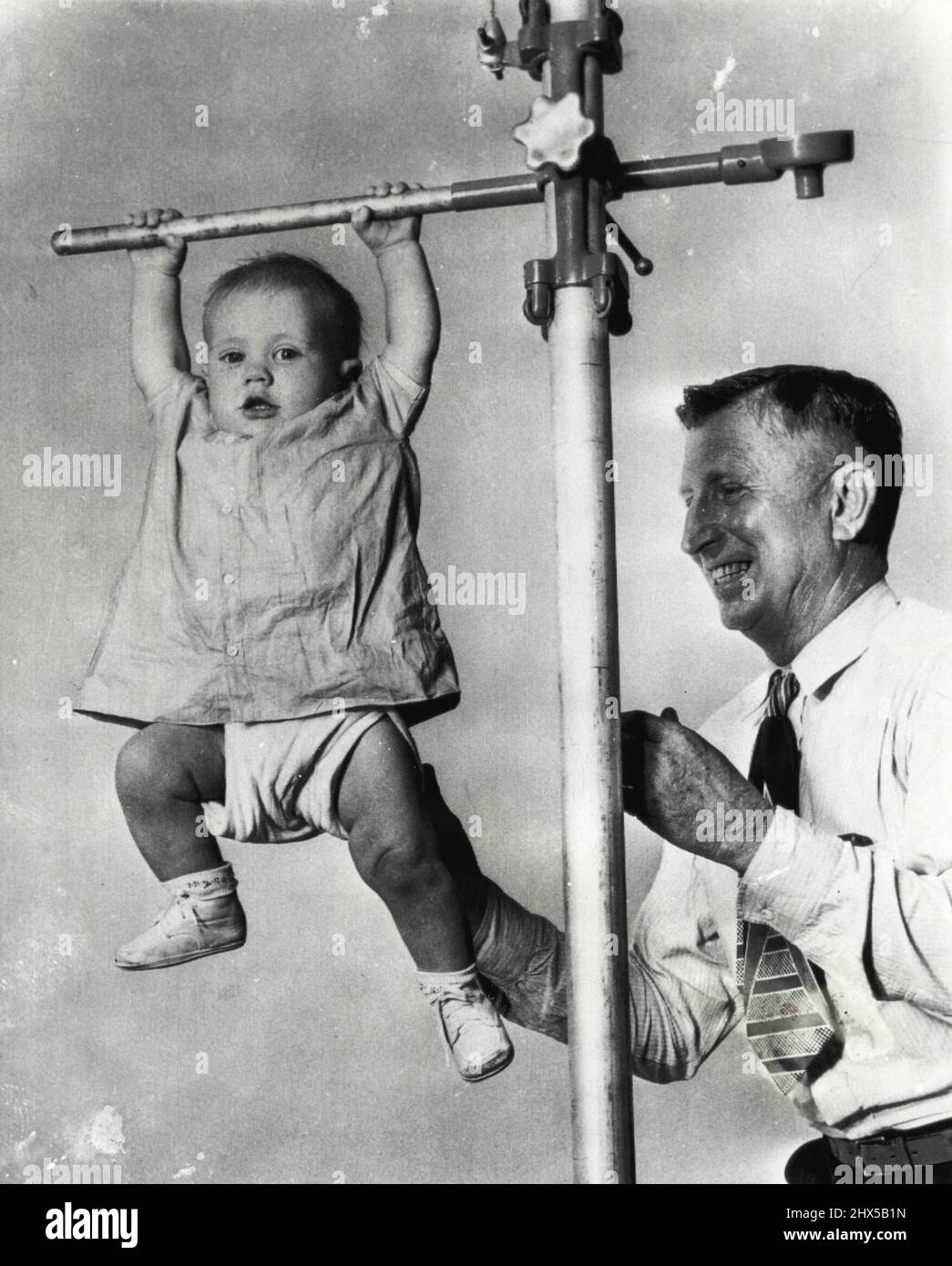 'Hey Pop, Look At Me!' - 7-months-old Larry Lynn Everett, of Athens, Tex., hangs from a horizontal bar as he performed for photographers here today. The 22-pound athlete does somersaults, mid-air backbends and balancing acts. His father, Bennie Everett (right), says Larry stood up in his crib at the age of 3 weeks. Recording to his father, Larry inherited his athletic ability from his mother, who is of Indian descent. Everett said, 'When she was a girl, ***** would almost outrun a deer.' January 17, 1950. (Photo by AP Wirephoto). Stock Photo