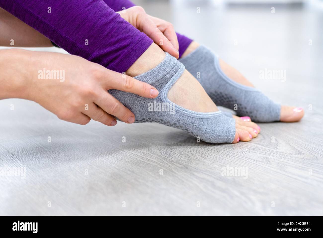 Close up Woman in purple leggings putting on her grey socks. Lady prepare for yoga workout. Concept of yoga accessories  Stock Photo