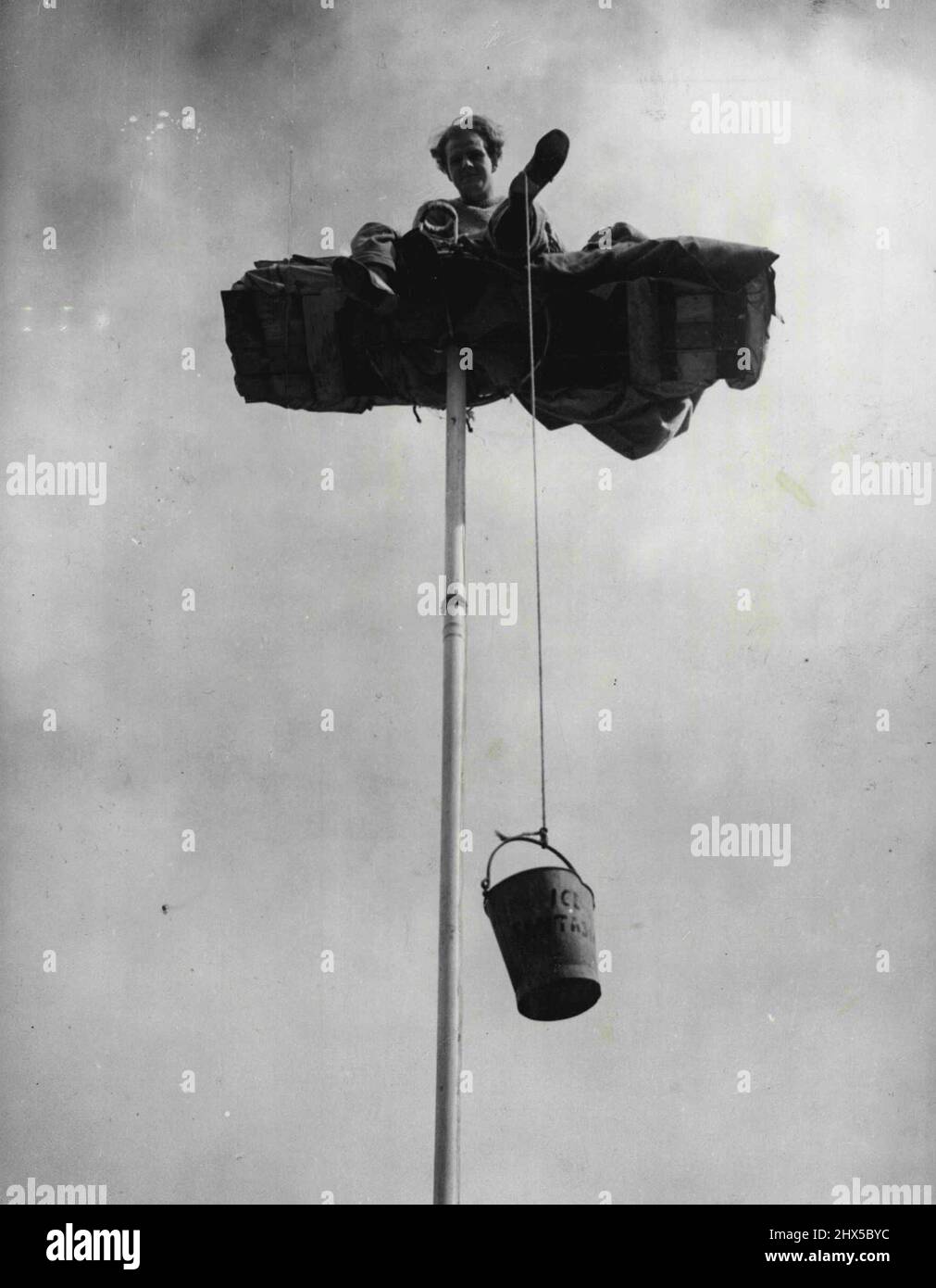 Reno Wons Be Parted from His Pole -- Because Reno (in private life 26- - year-old acrobat John Fossett) refuses to come dawn from his perch atop a 40-feet-high flag-poles his food has to be sent up by rope and bucket, as this picture taken of Britain's high-est striker at Brighton (Sussex) Zoo - today (Friday) shows. Reno shinned up the pole yesterday morning, after Mr. Vic Templer producer of the Zoo's summer ice revue refused to release him from his contract. Normally, Reno does aerial acrobatics on the pole. Now, he just sits-despite appeals, despite the weather. He says he won't come down Stock Photo
