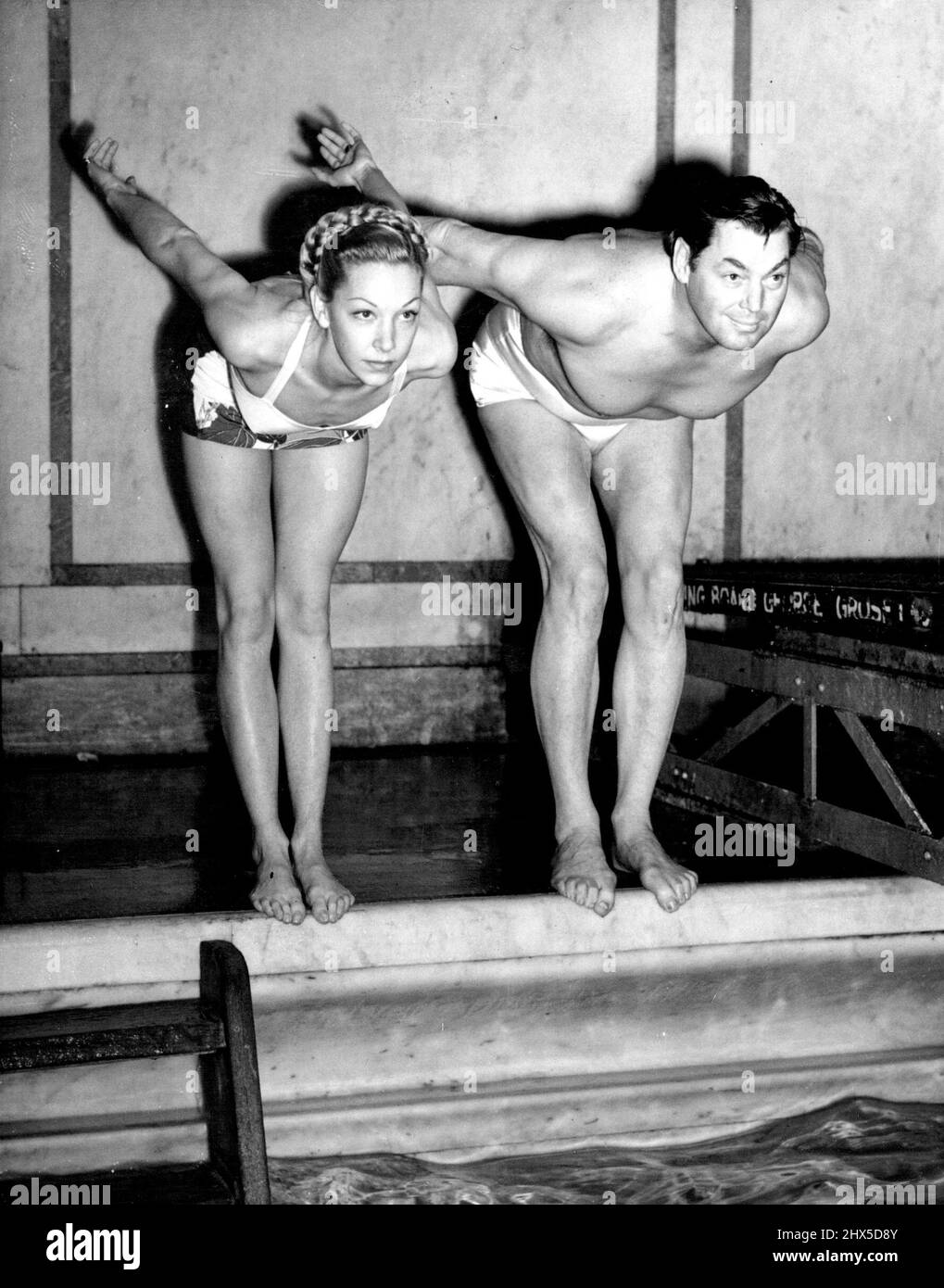 In Time With 'Tarzan' In perfect rhythm 'Tarzan' and his 'Mate'-screen stars Johnny Weismuller and Belita go off the pool-side together, as they rehearse in London to-day, (Monday), for their forthcoming roles in the Aqua show at Earls Court. February 16, 1948. Stock Photo