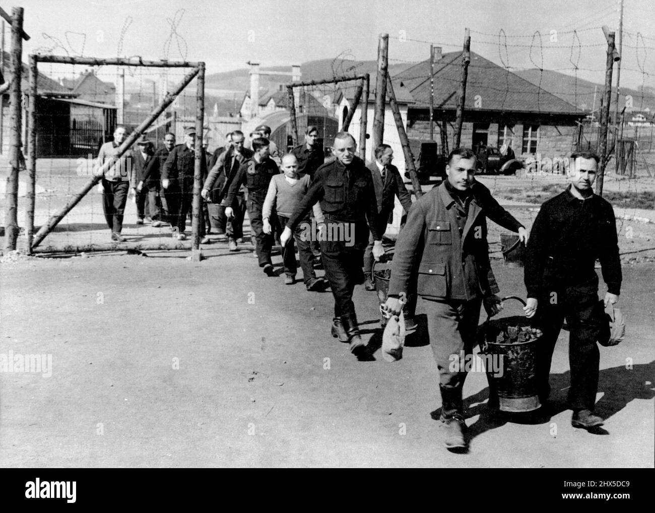 Life in an Internment Camp for German Nazis. A working party of Nazi internees returning with buckets of coke for the kitchens through the gates of Camp Roosevelt, Hemer, Germany. At Hemer, in the British-occupied zone of Germany, 3,300 Nazis (mostly Gestapo and S.S. men) are interned in Camp Roosevelt, formerly a German prisoner-of-war camp Stalag 6b. The internees have their time fully occupied, because,in addition to their instructional centre where they are taught everything from dramatic art to brick-laying, they have all the camp chores to perform, such as working on the allotments and f Stock Photo