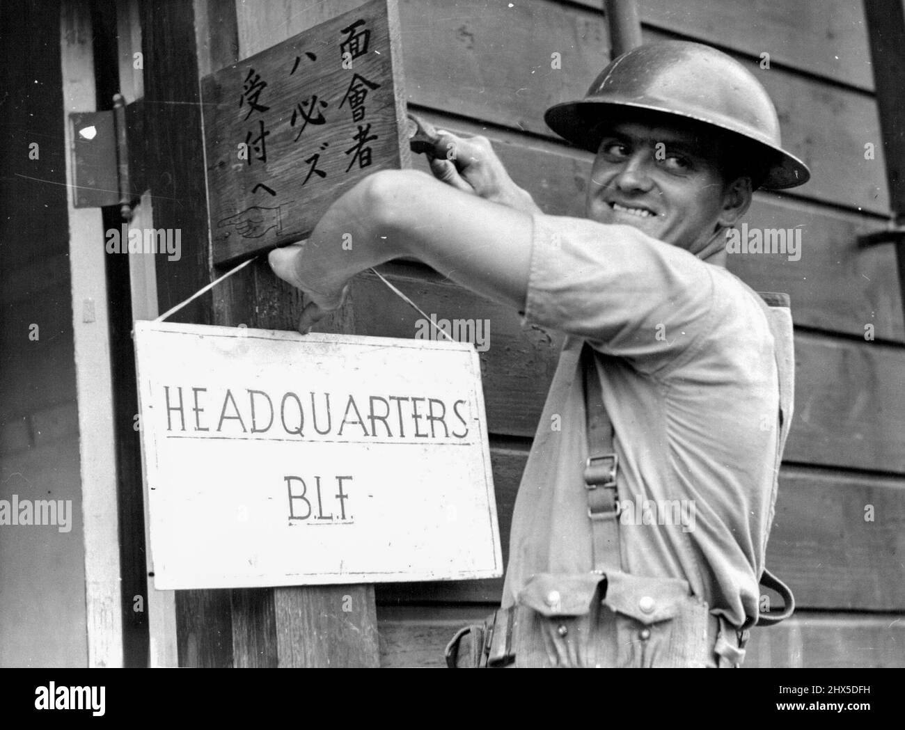 Able Seaman Steve Clough of Lakemba, N.S.W. smiles broadly as he tacks up the British Landing Force Headquarters sign on the entrance to the building requisitioned for this purpose in the Yokosuka Naval Base. September 16, 1945. (Photo by Australian Official Photo). Stock Photo