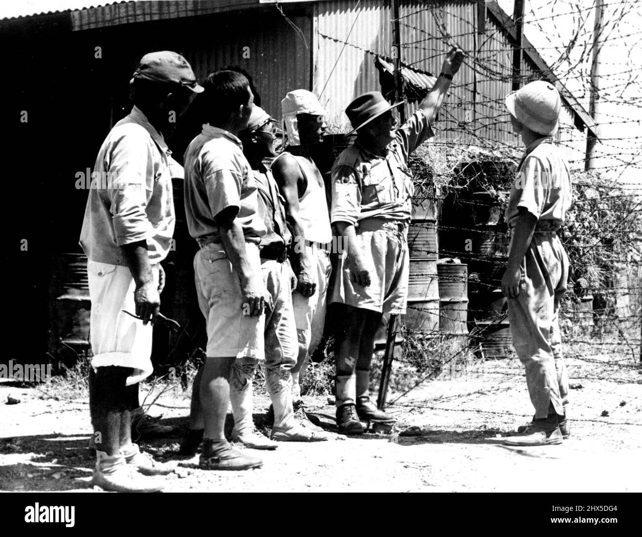 An Australian N.C.O. gives orders to Japs who have been brought from Timor as a working party. They are building a barbed wire enclosure for Jap war criminals at present on trial in Darwin. March 13, 1946. (Photo by Australian Official Photograph). Stock Photo