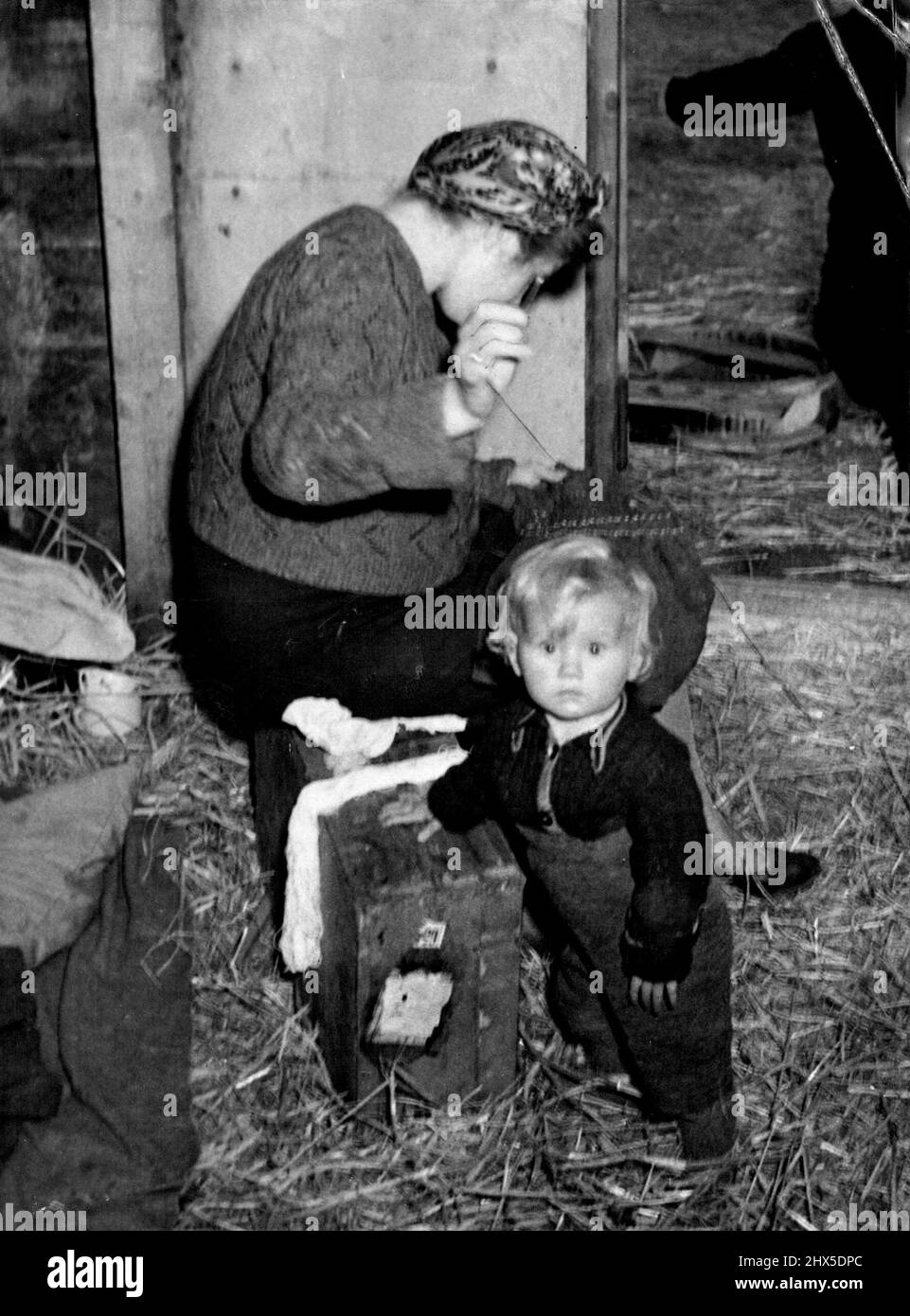 The Menace of Starving Europe Stables Make Transit Camp For Displaced Germans Travelling West In British Zone -- A German woman sits by the doorway doing her mending, while her child stumbles about in the straw of their stable in Velzen camp, 25 miles from Luneberg, in British occupied Germany. This will be their home until they can join a trainload of other refugees going to one of the better-fed country districts. German families from the border zone between British and Russian occupied territory, who have been evacuated to take way for Germans expelled from Poland and the eastern territorie Stock Photo
