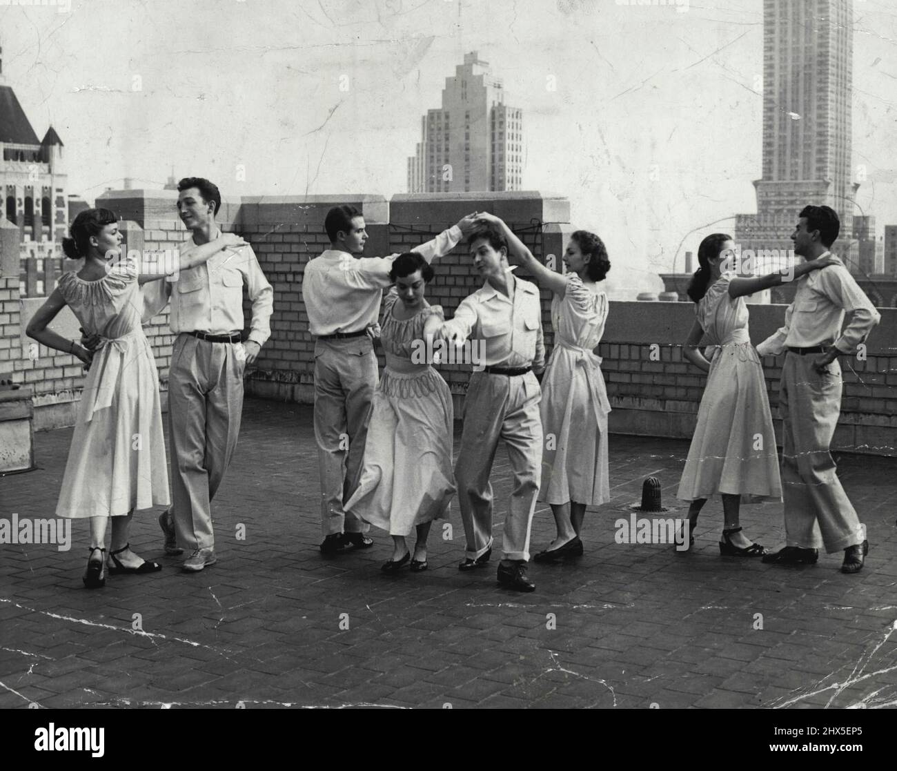 The square dance craze has hit many suburban homes. When there's not enough room inside, or just for the fun of it, square dancers adjourn to the roof, where they square among festoon lights and washing lines. June 29, 1950. (Photo by Paul Schumach, Metropolitan Photo Service). Stock Photo