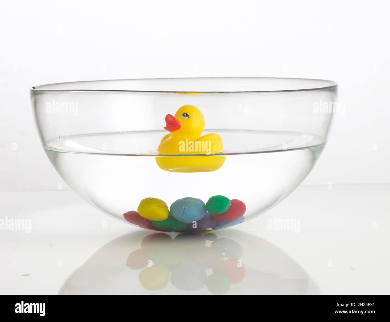 Rubber duck floating on water and colourful clay balls at bottom of bowl Stock Photo