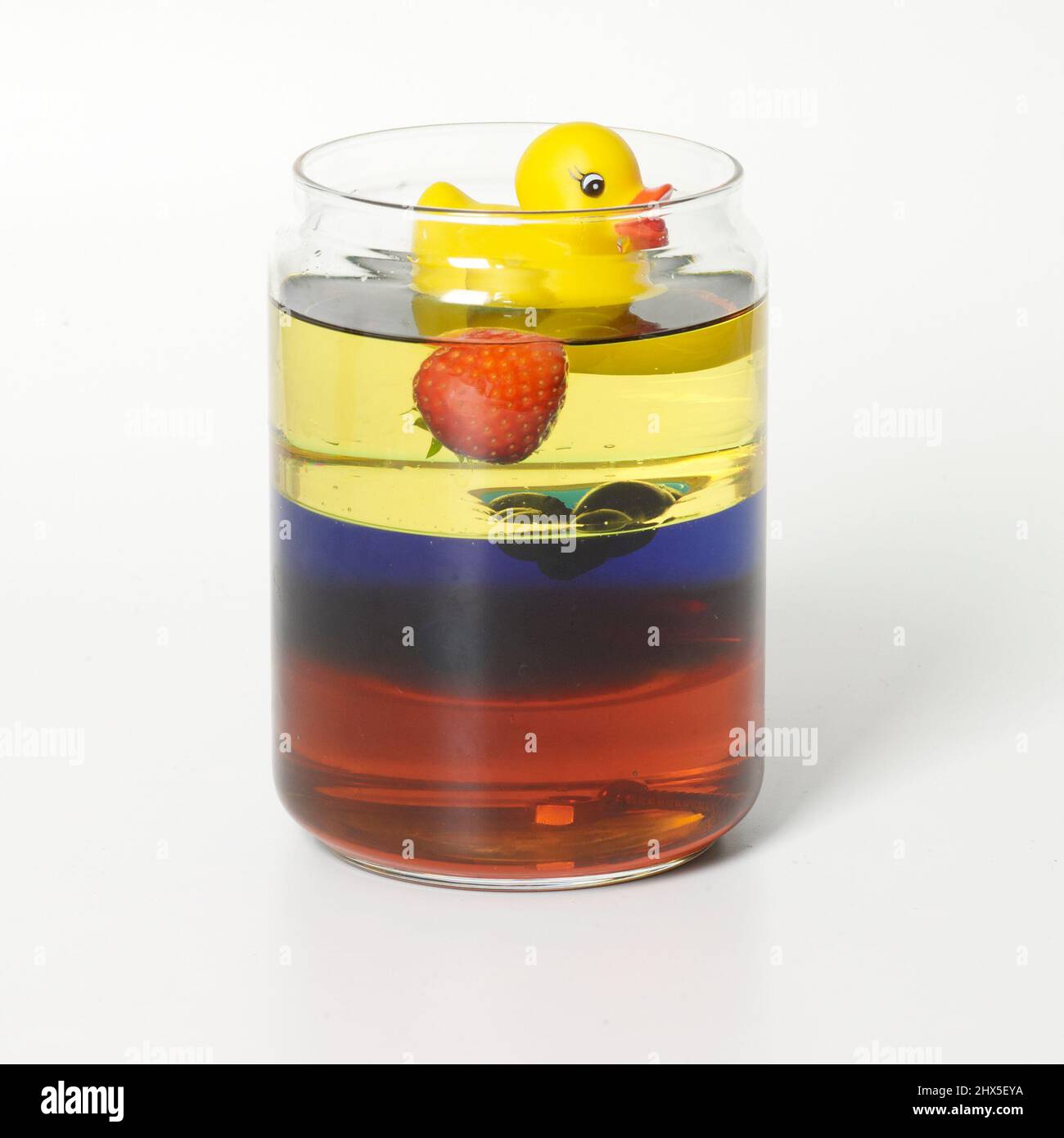 Layers of liquids in glass jar with rubber duck and strawberry floating on top Stock Photo