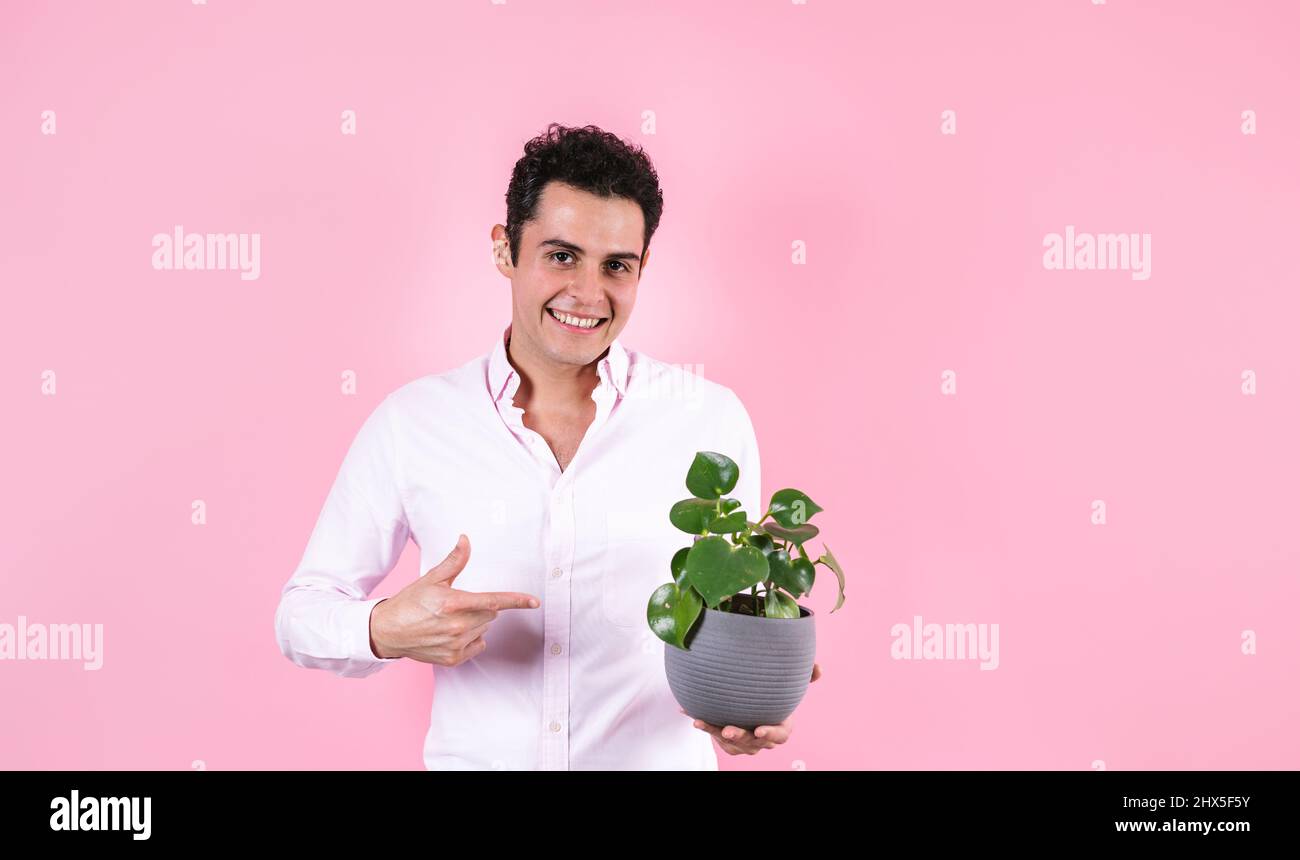 young hispanic man holding a green plant and smiling at camera on pink background in Mexico Latin America Stock Photo