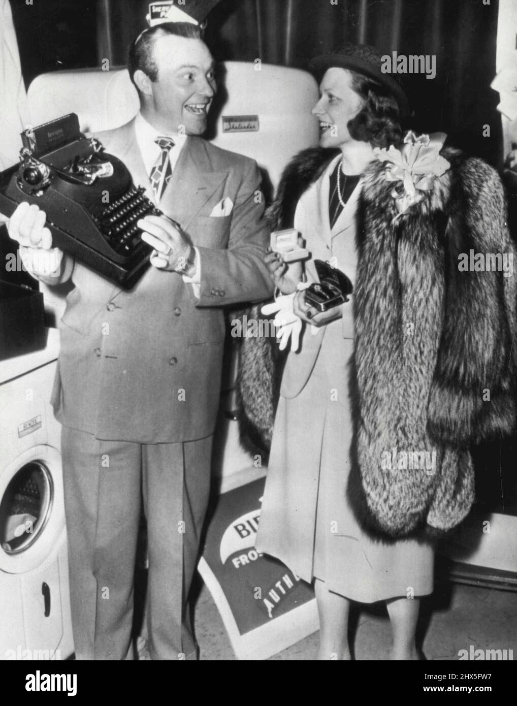 Hush Money -- Mrs. William McCormic, Lockhaven, Pa., housewife who identified ex-film actress Clara Bow as 'Mrs. Hush' to win a radio contest, receives some of the $17, 000 worth of prizes from program director Ralph Edwards. Here today. She holds a diamond and rugy wristwatchk, a diamond ring and wears a fur coat. In background is a washing machine and a refrigerator. March 22, 1947. (Photo by AP Wirephoto). Stock Photo