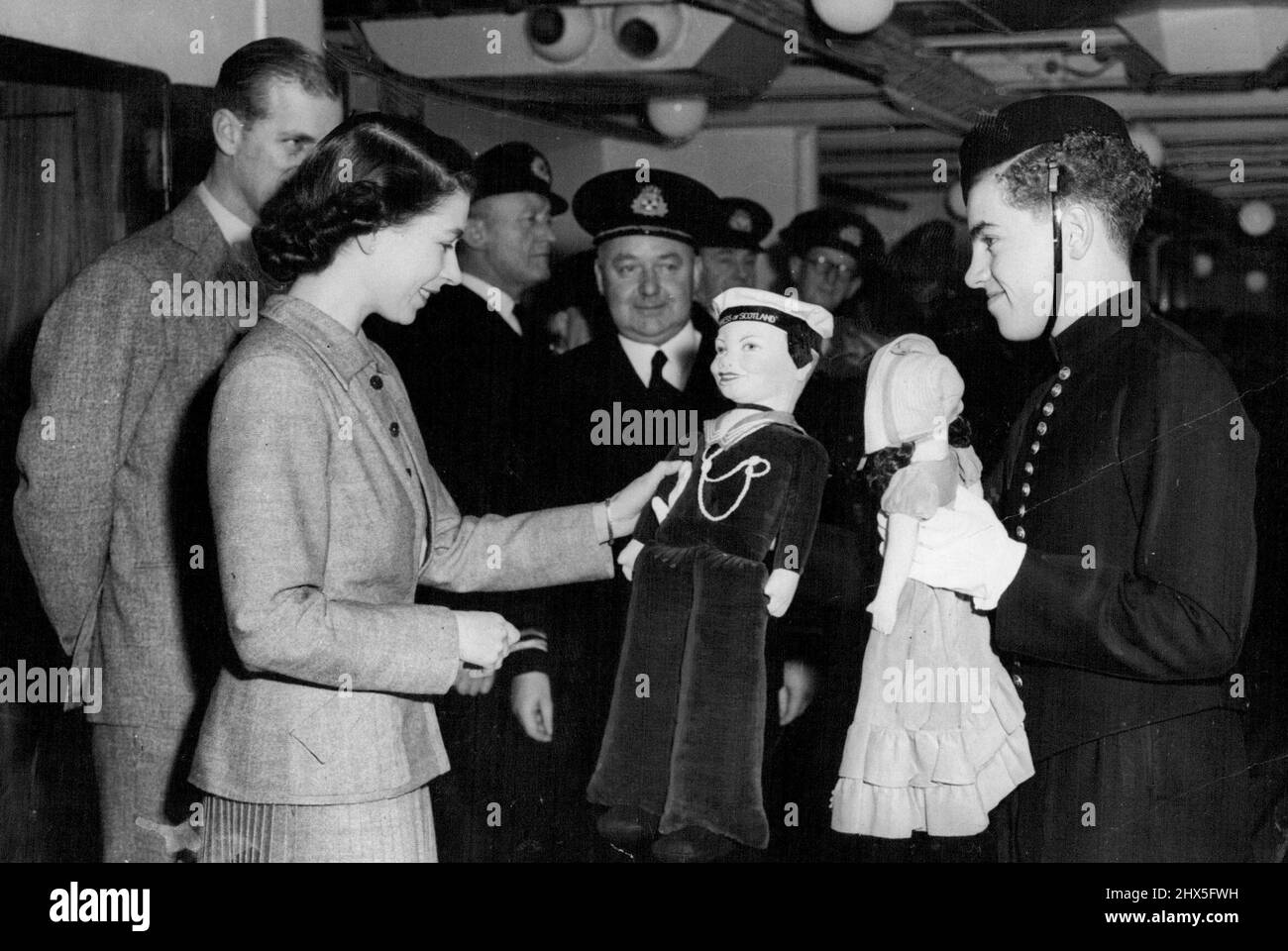 The Princess During Atlantic Crossing Special Pictures By S. Devon -- George Newcombe, Senior Beld boy on the ship, Presenting to Princess Elizabeth two dolls for Princess Anne and Prince Charles which were subscribed for be the ship's company. Also in the picture are the Duke of Edinburgh and Capt. C. E. Duggan, master of the 'Empress of Scotland'. Photographers released today show Princess Elizabeth during her trip from Canada on the S.S. 'Empress of Scotland' in which she landed at Liverpool yesterday. November 18, 1951. (Photo by Paul Popper). Stock Photo