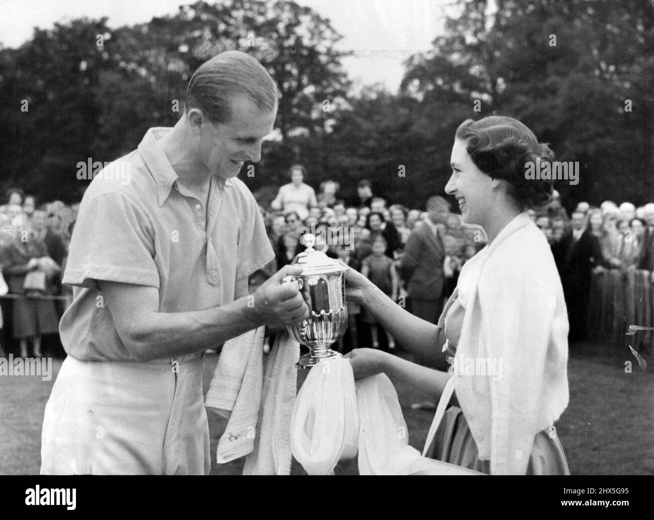 From The Princess To The Duke -- Princess Margaret, in turquoise blue dress and white cardigan, smiles as she present the Duke of Sutherland cup to the Duke of Edinburgh after the Cowdray park team had beaten the greyhounds in the final at the polo tournament at Cowdray park Midhurst Sussex, to-day. (Whit-Monday). The Princess had driven down with the Duke from Windsor. June 07, 1954. (Photo by Reuterphoto). Stock Photo