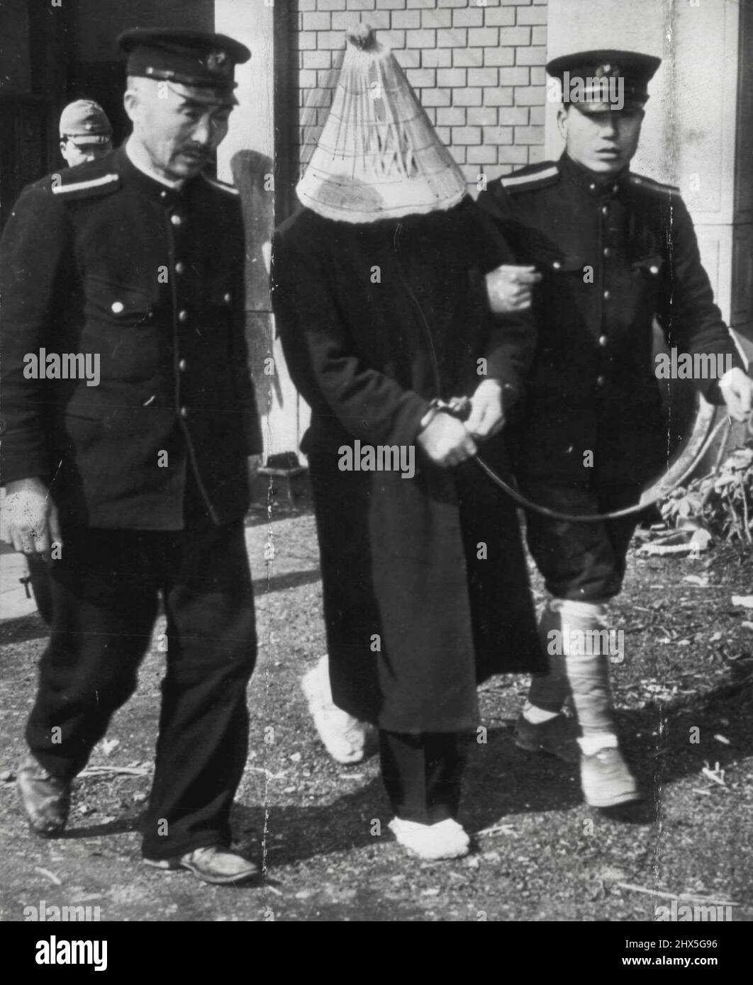 Japanese 'Bluebeard' Goes To Court - Flanked by two policemen, one of whom holds the traditional rope attached to the prisoner's handcuffed wrists, Yoshio Kodaira, 43, is taken to court in Tokyo to face charges that he was responsible for the deaths of 10 women. Under Japanese law the straw hat he wears is allowed to hide his shame. March 14, 1947. (Photo by AP Wirephoto). Stock Photo